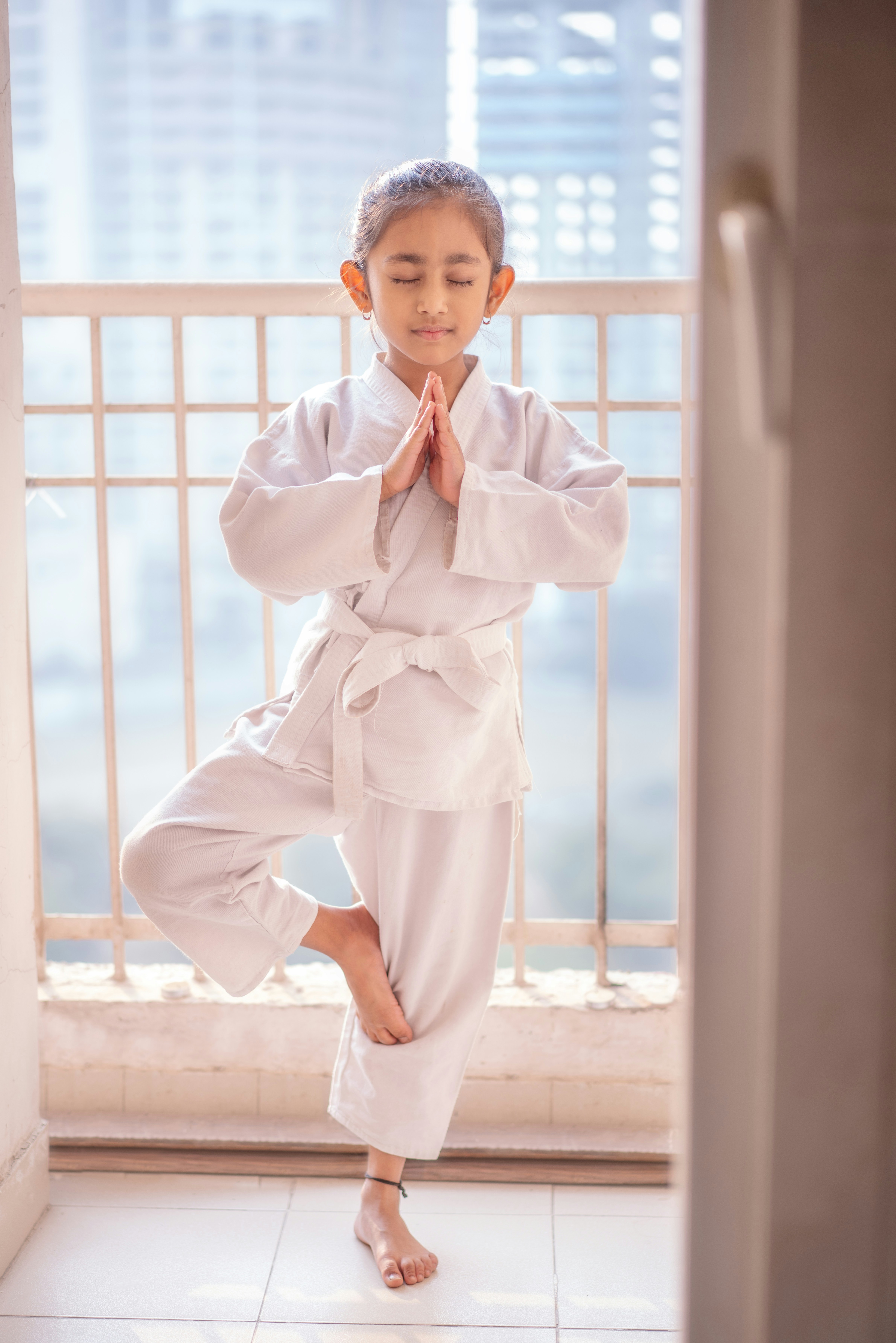 Young girl in white gi practices tree pose yoga.