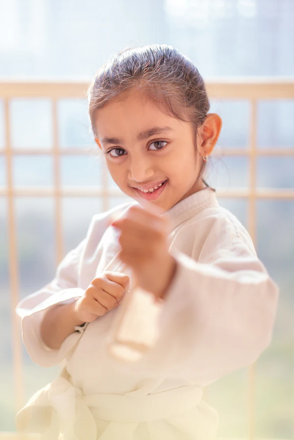 A smiling girl in a karate gi holding up a fist