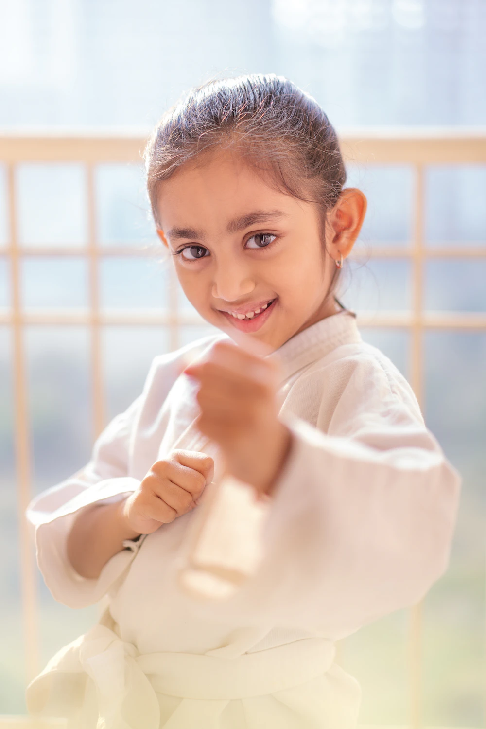 A smiling girl in a white gi with her fists up, ready