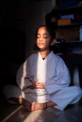 Young girl in white gi meditating with eyes closed.