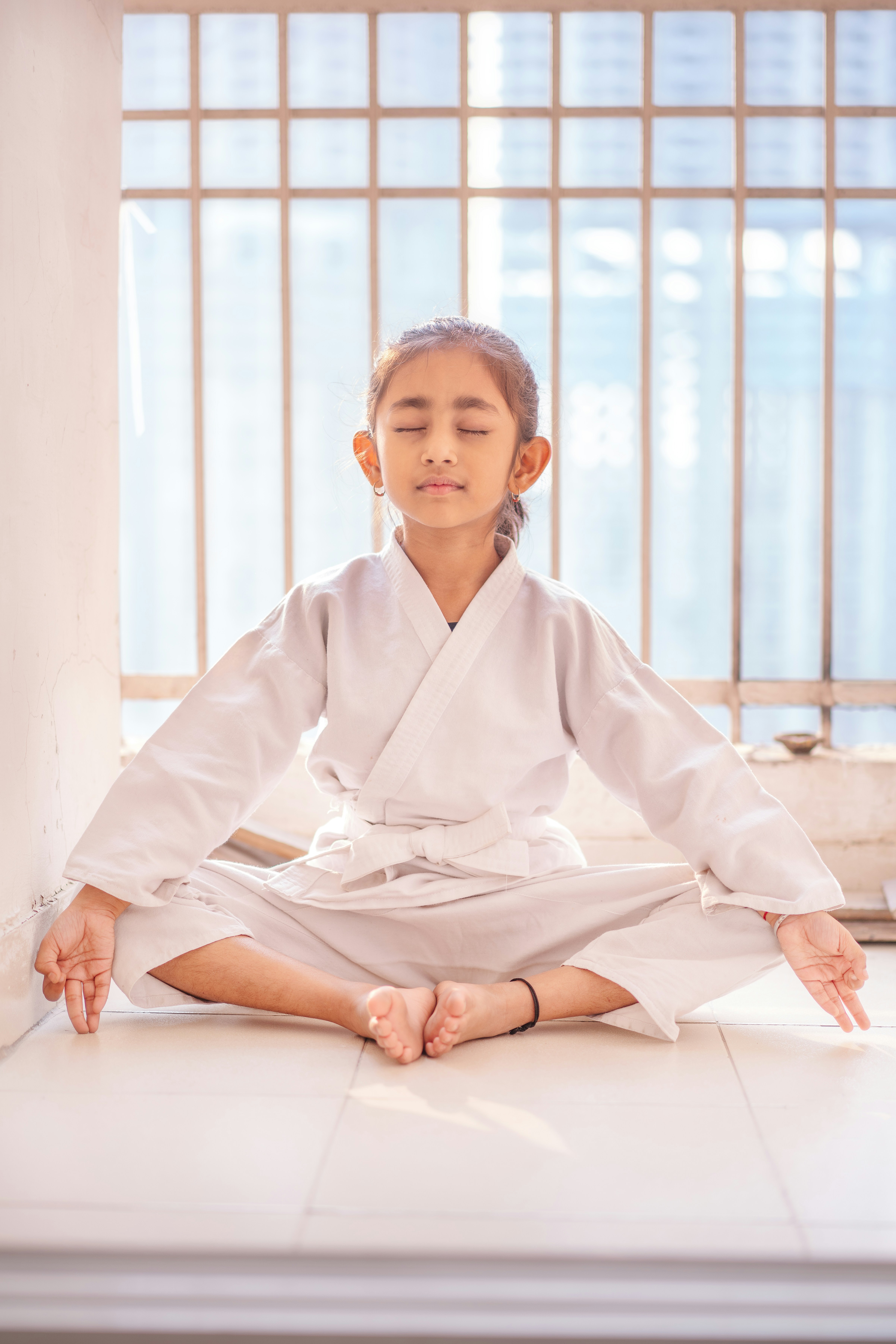 Young girl in white gi meditating with eyes closed.