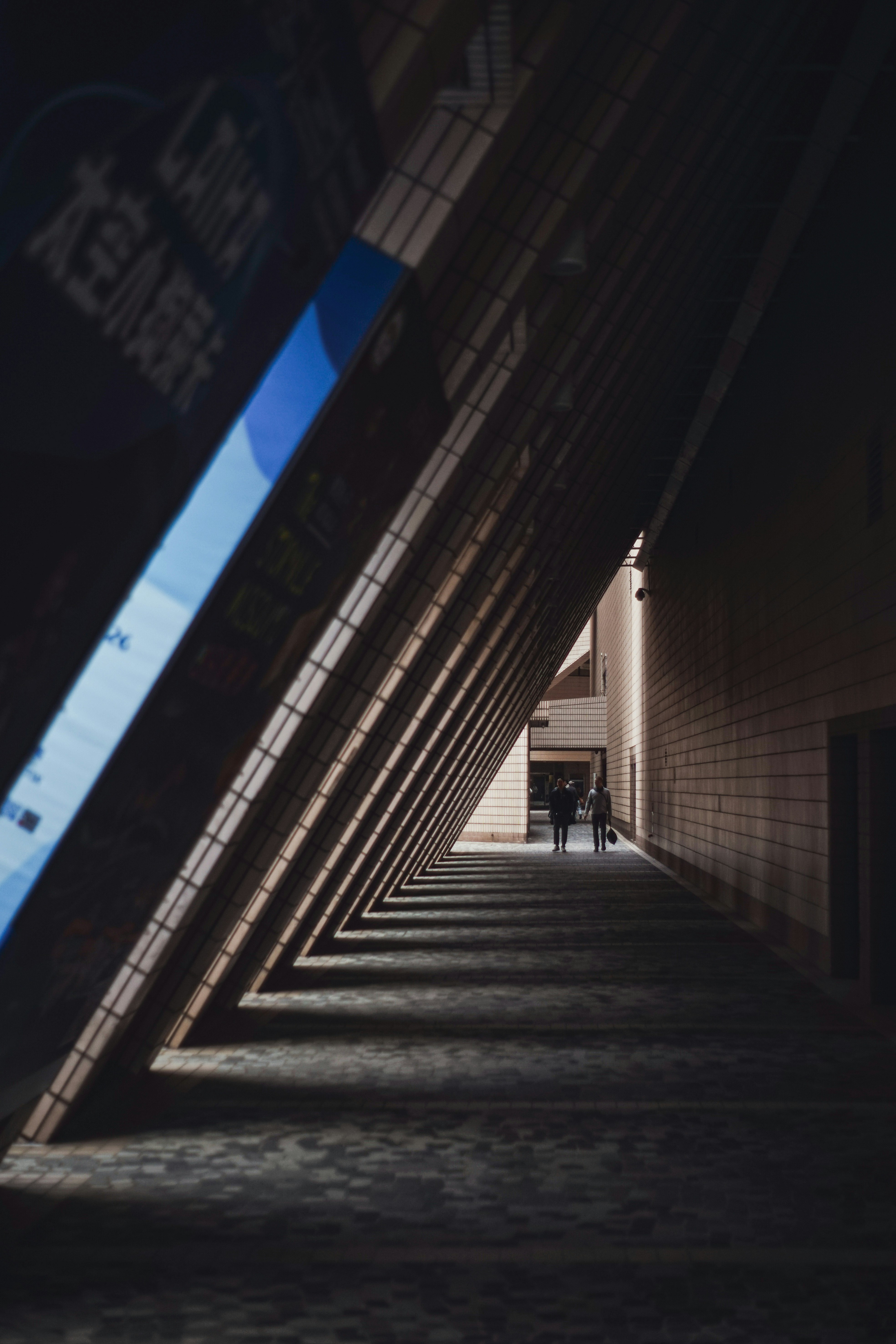 Two people walk down a shadowed hallway with angled ceiling