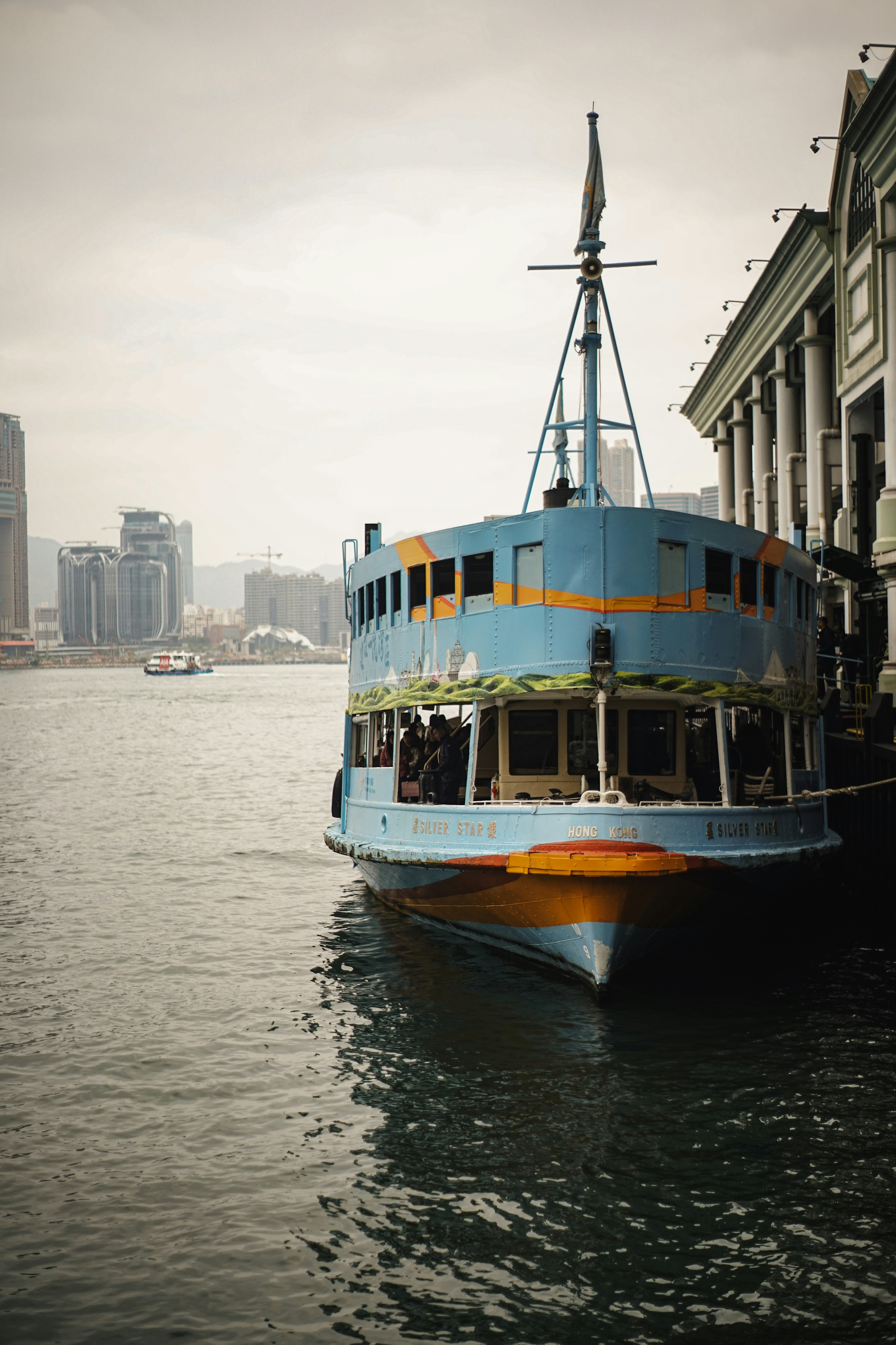 A blue ferry docked beside a building with cityscape.