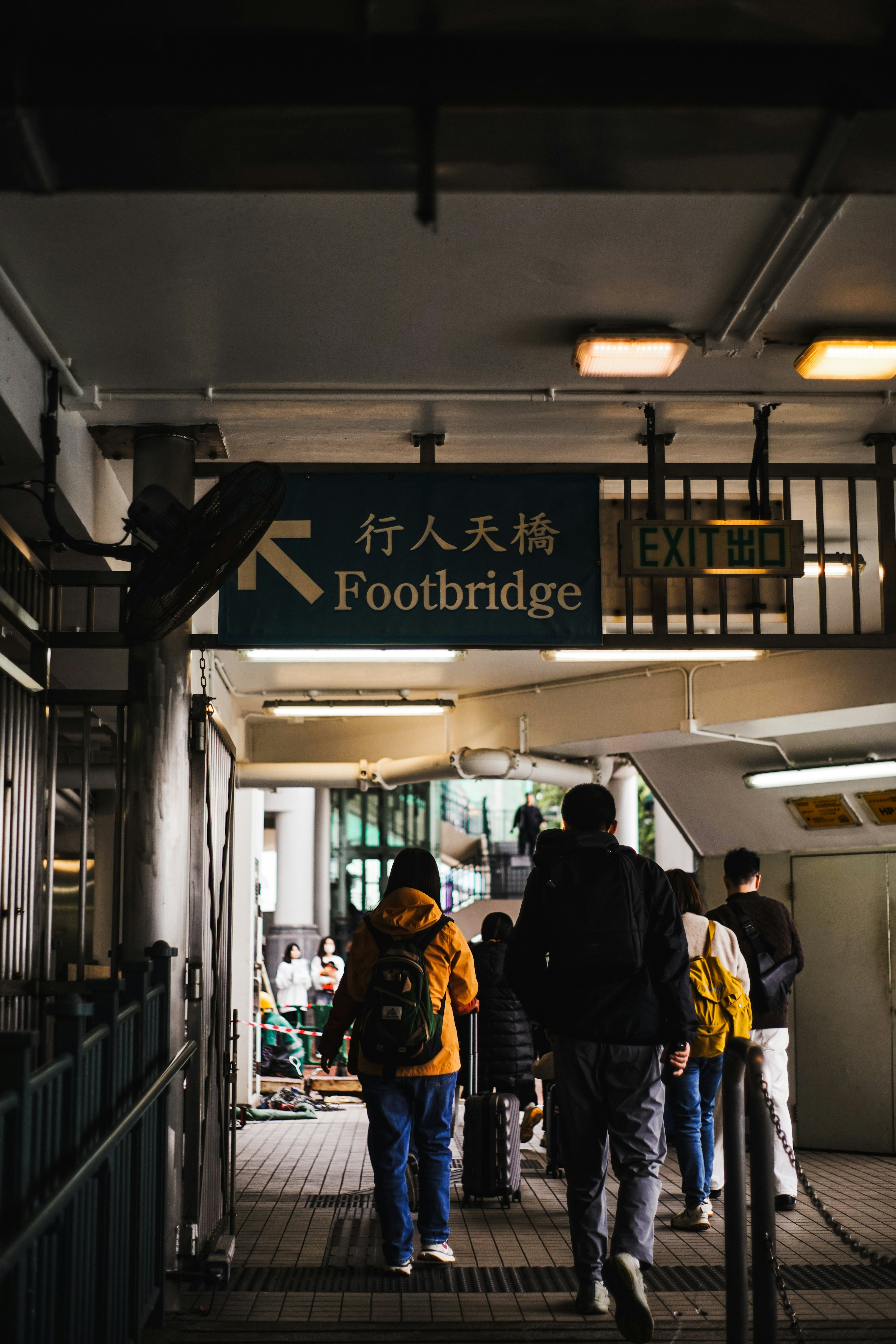 People walking up stairs towards a footbridge sign.