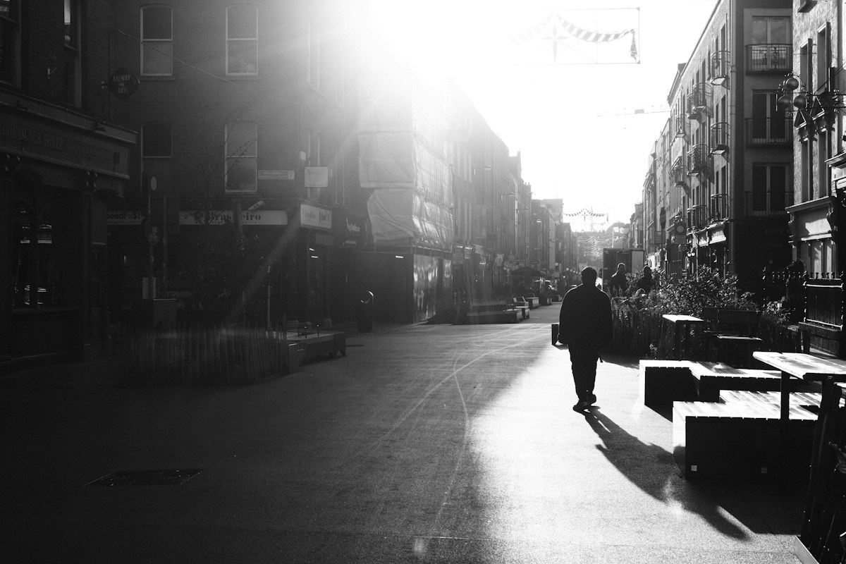 Silhouette d'un passant marchant dans une rue de ville baignée par le soleil du matin, en noir et blanc