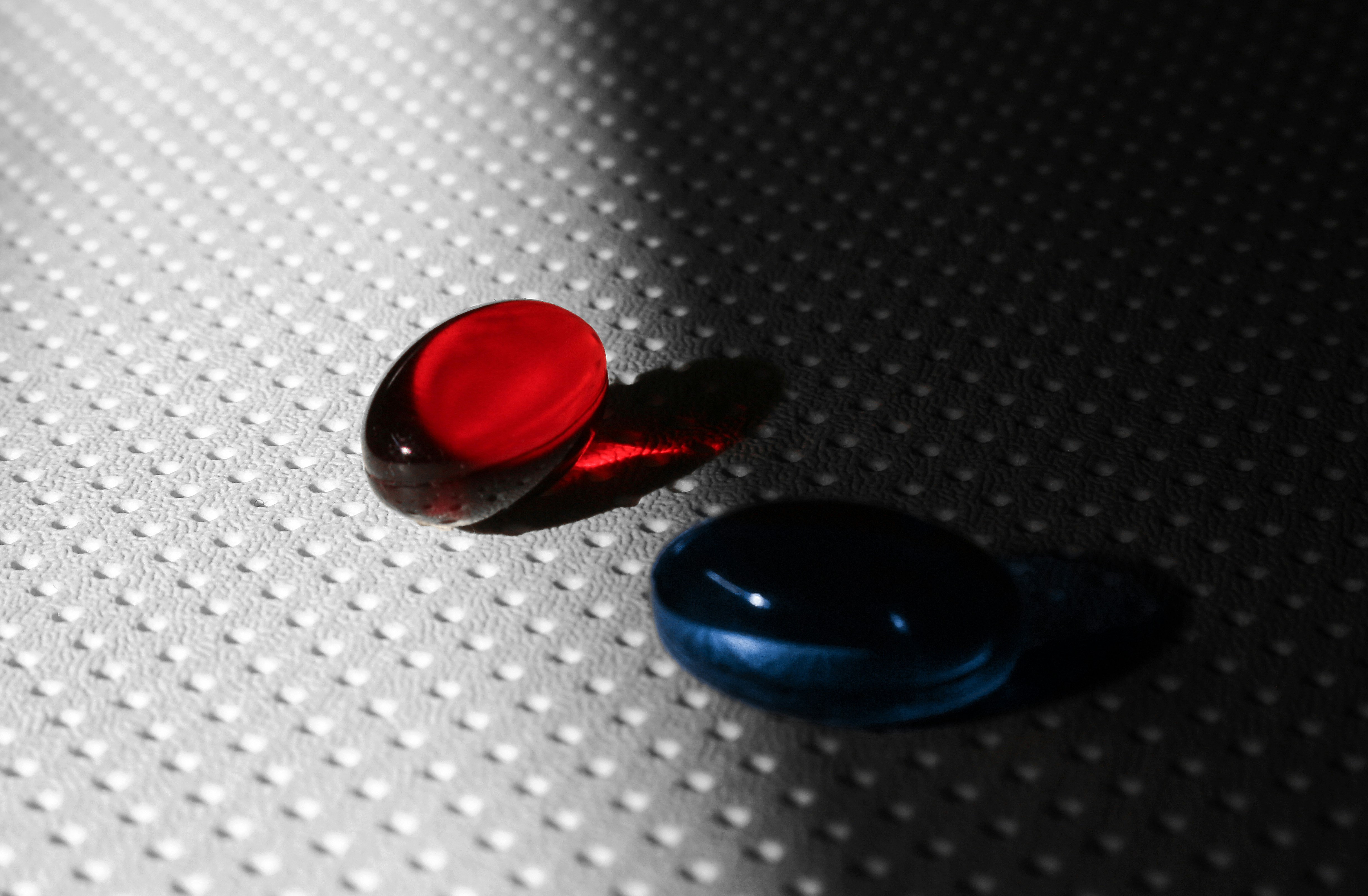 Two pills, red and blue, on textured surface.