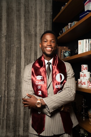 A smiling graduate wears a sash over his suit.