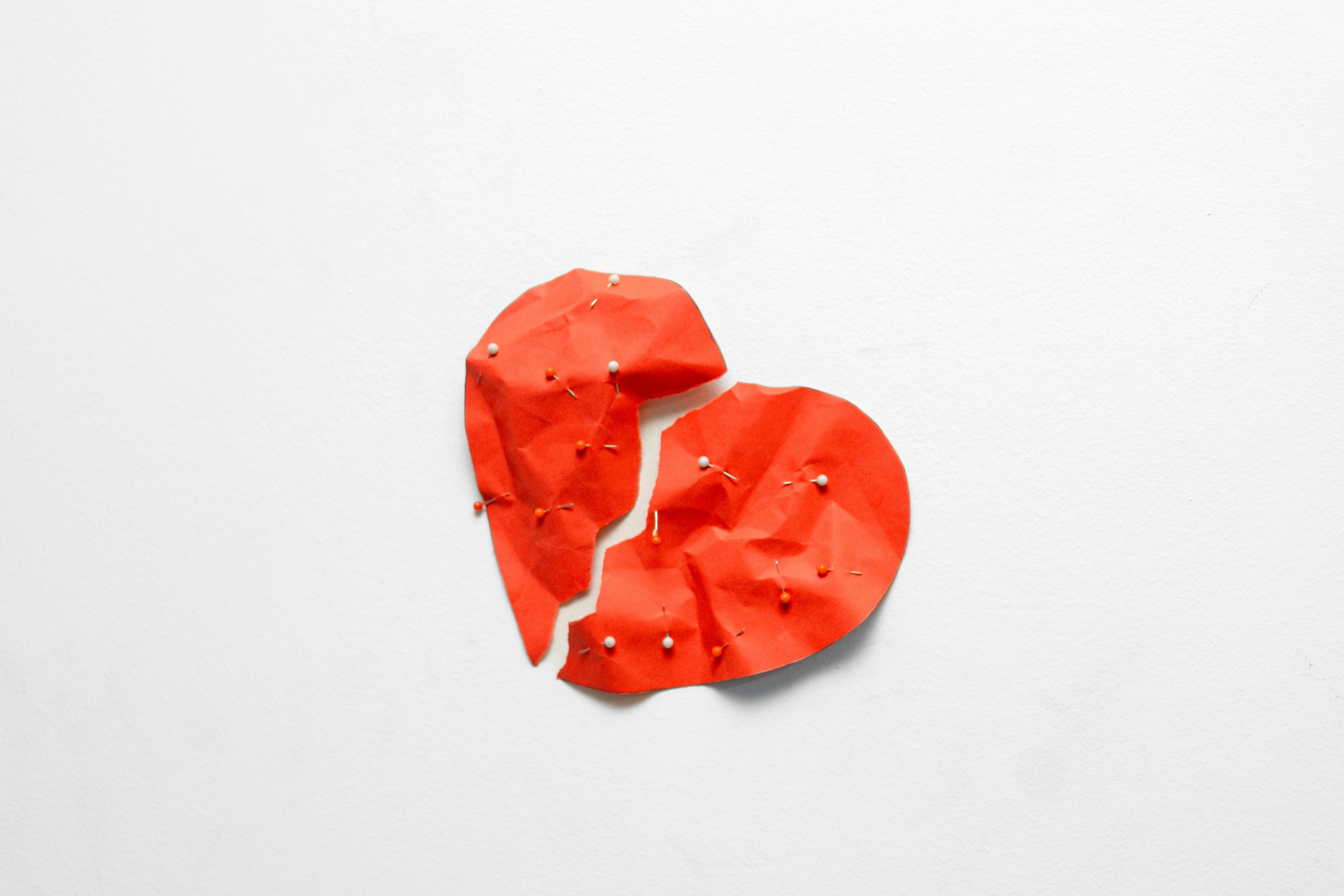 A broken red heart with pins on a white background