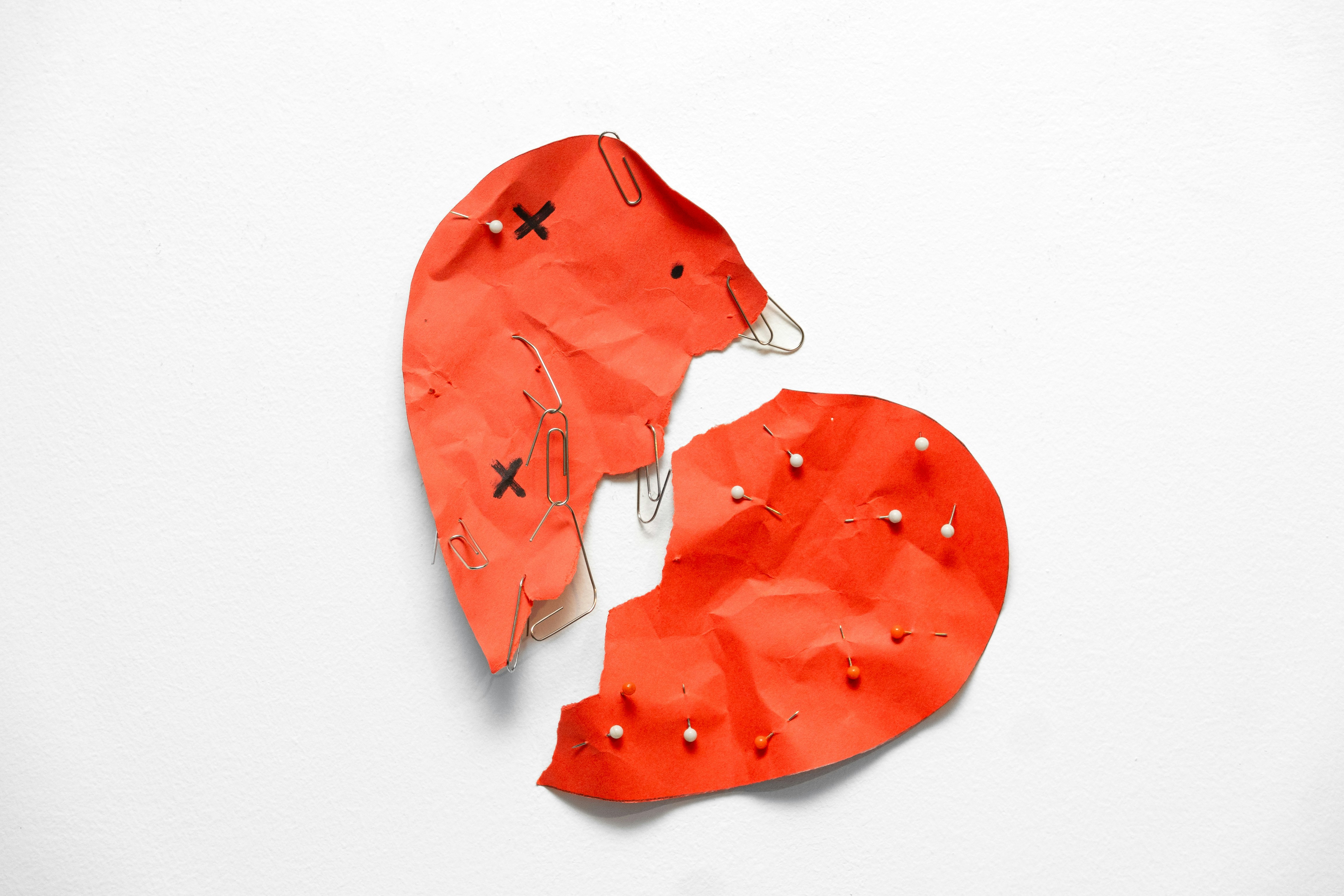 A broken red heart held together by pins.