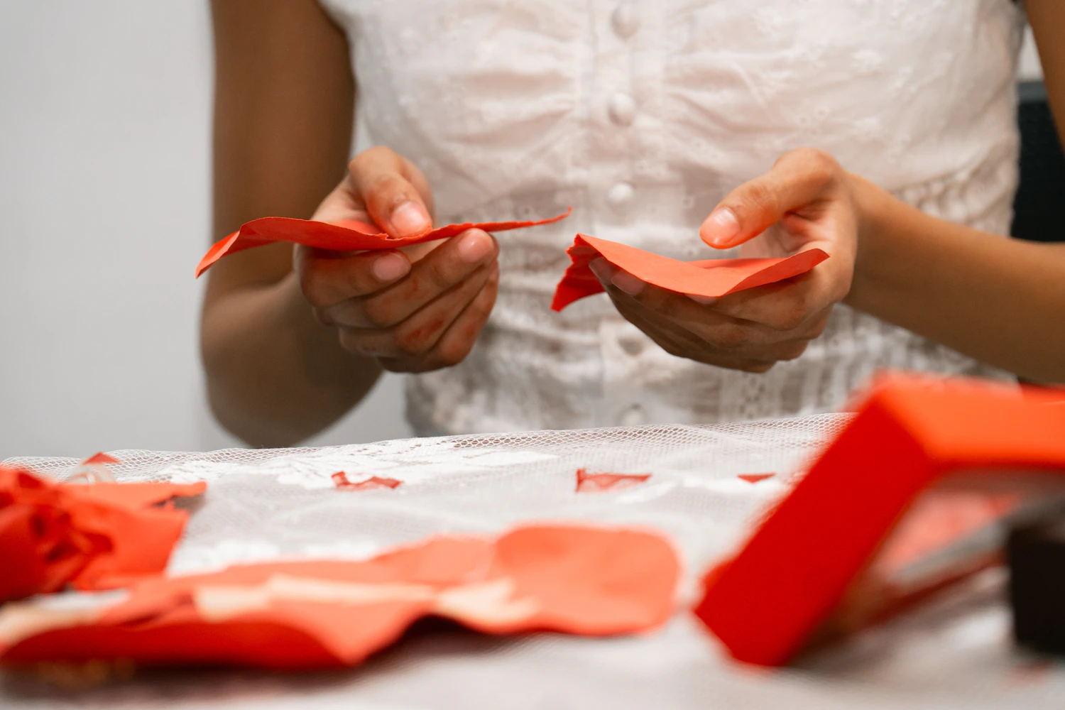 Hands folding red kami into cranes at a white worktable