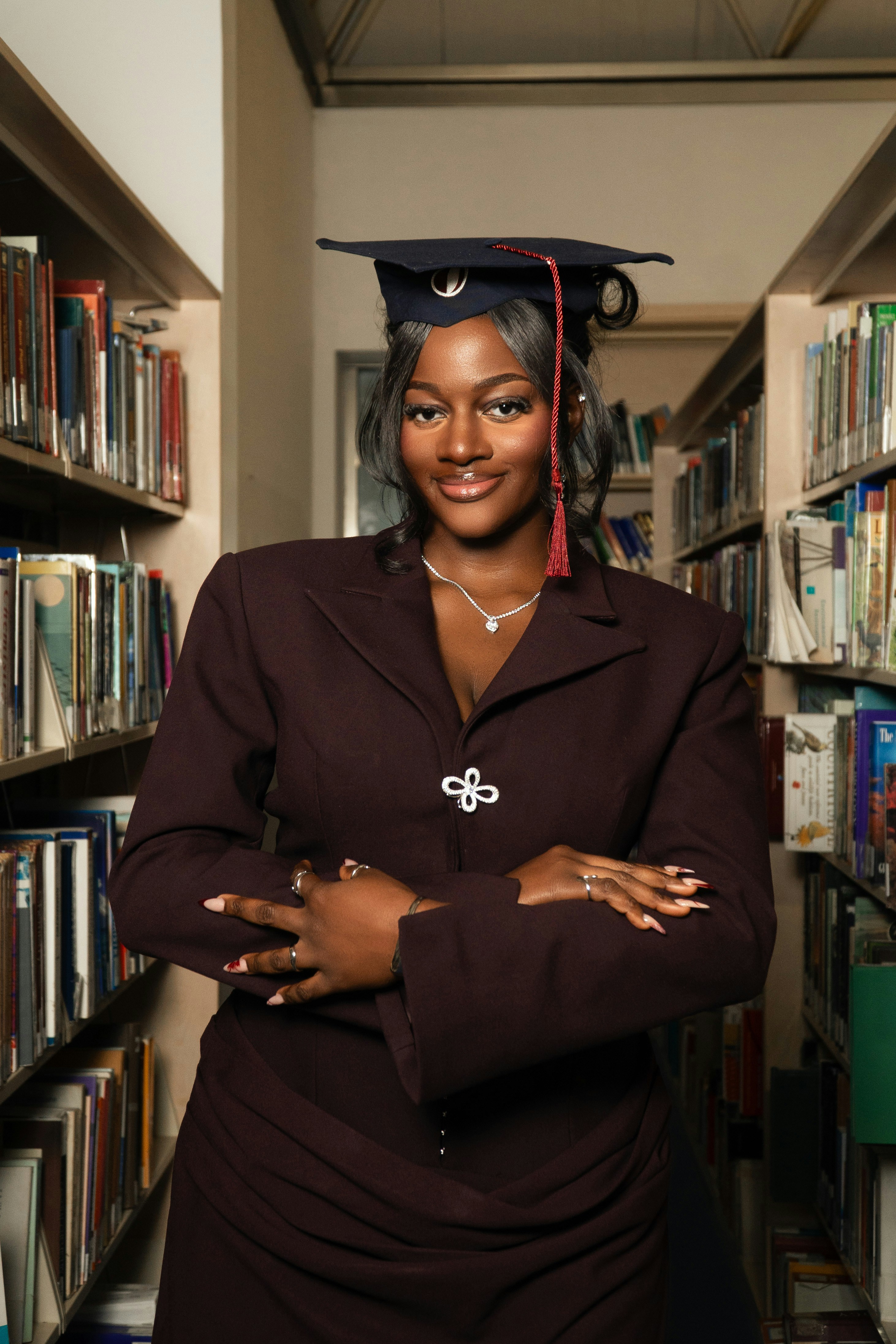 A smiling graduate in a blazer stands in a library.