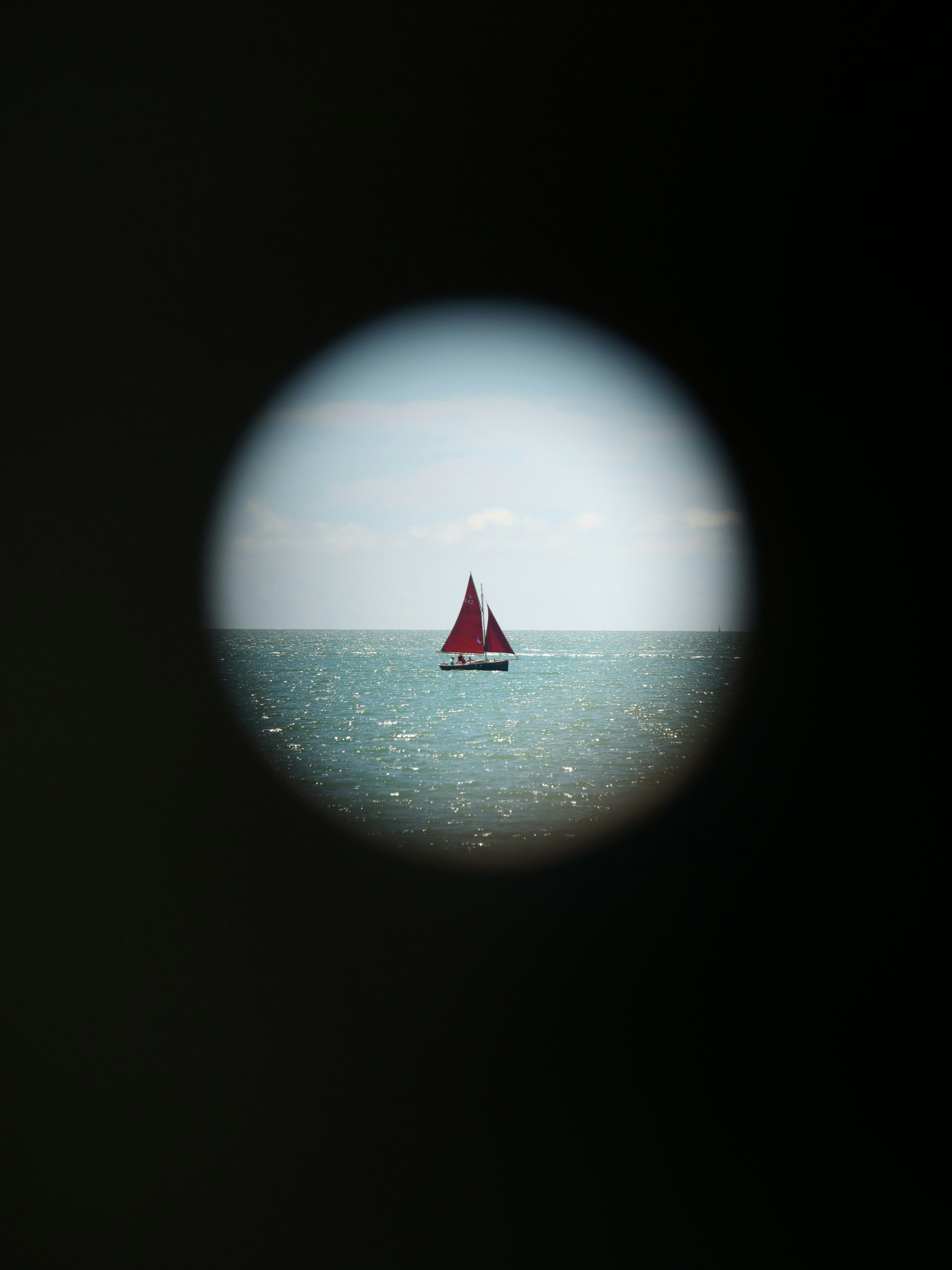 Red sailboat on the sparkling blue ocean