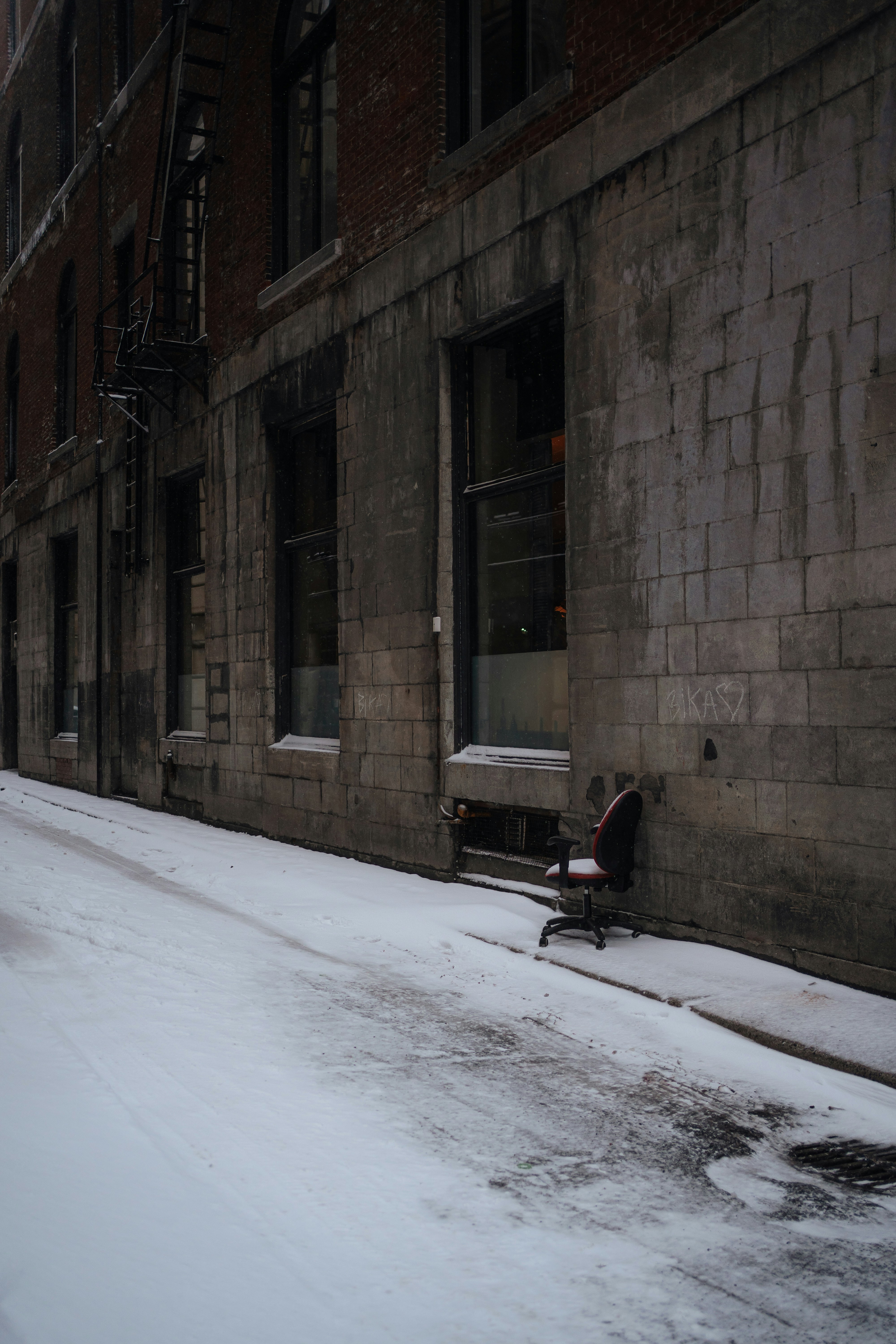 An empty office chair sits in a snowy alleyway.