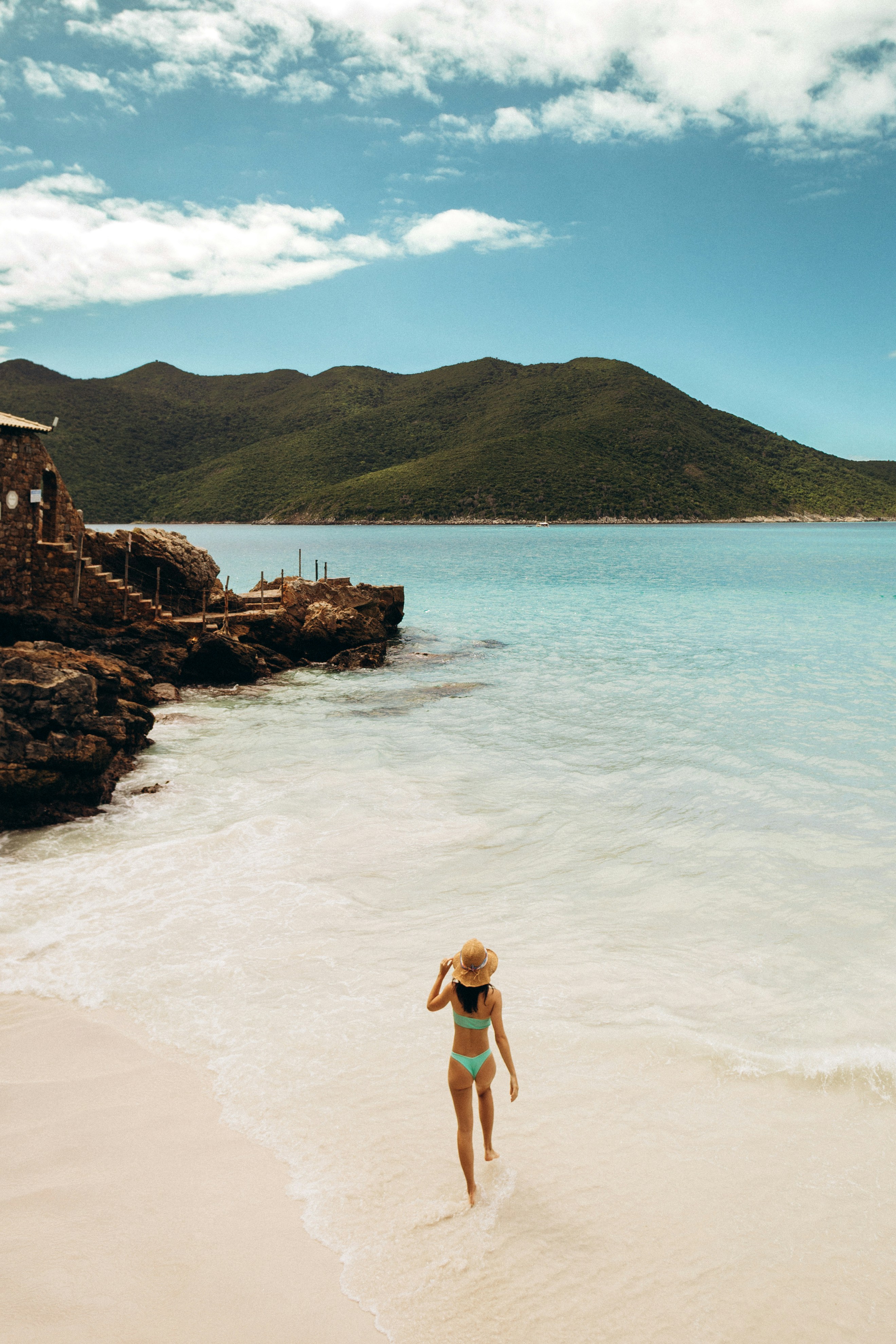 Woman in bikini walks on a sandy beach near ocean.
