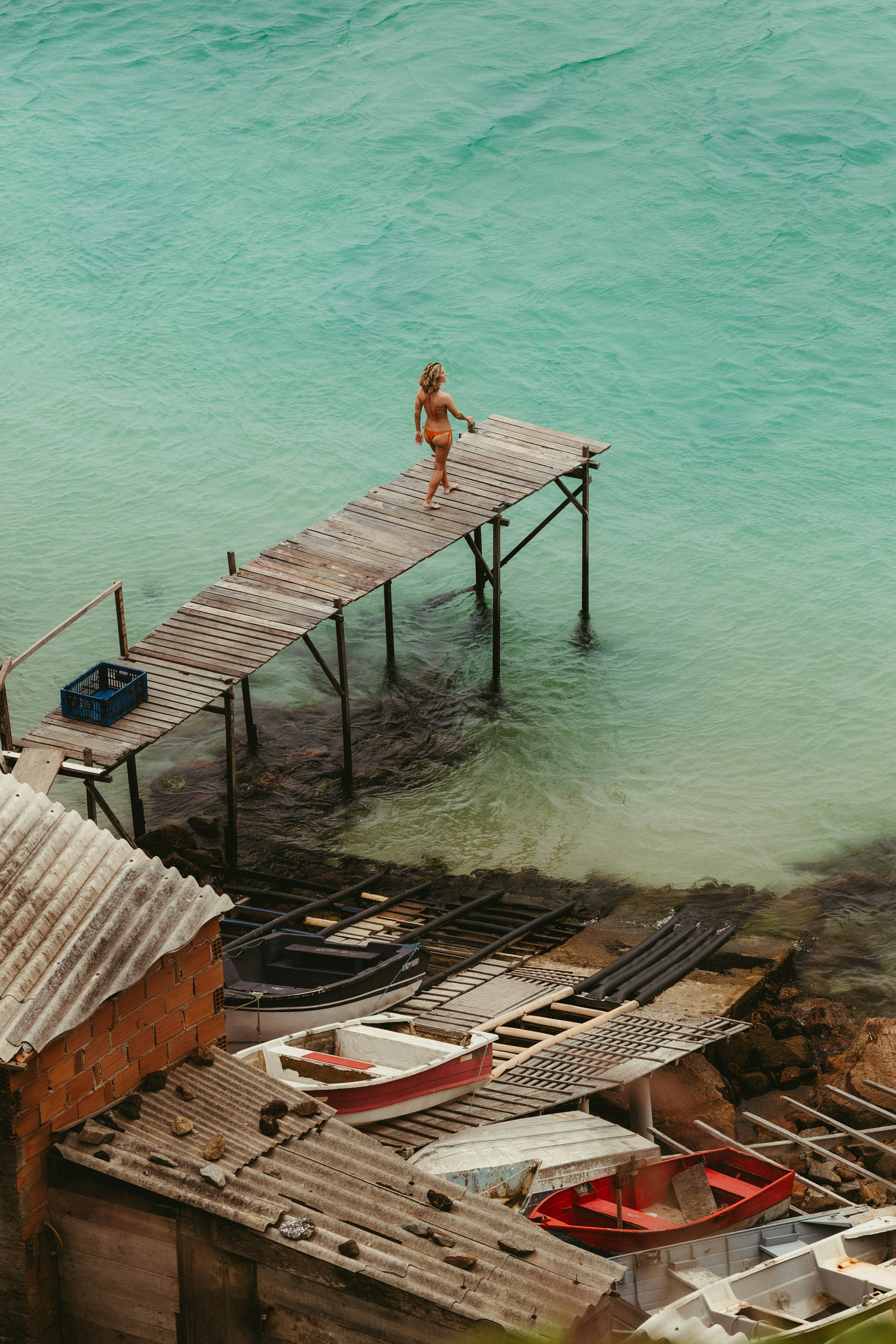 Una mujer camina sobre un muelle de madera sobre aguas turquesa.