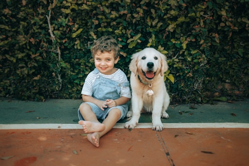 A smiling boy and a golden retriever puppy sit together.