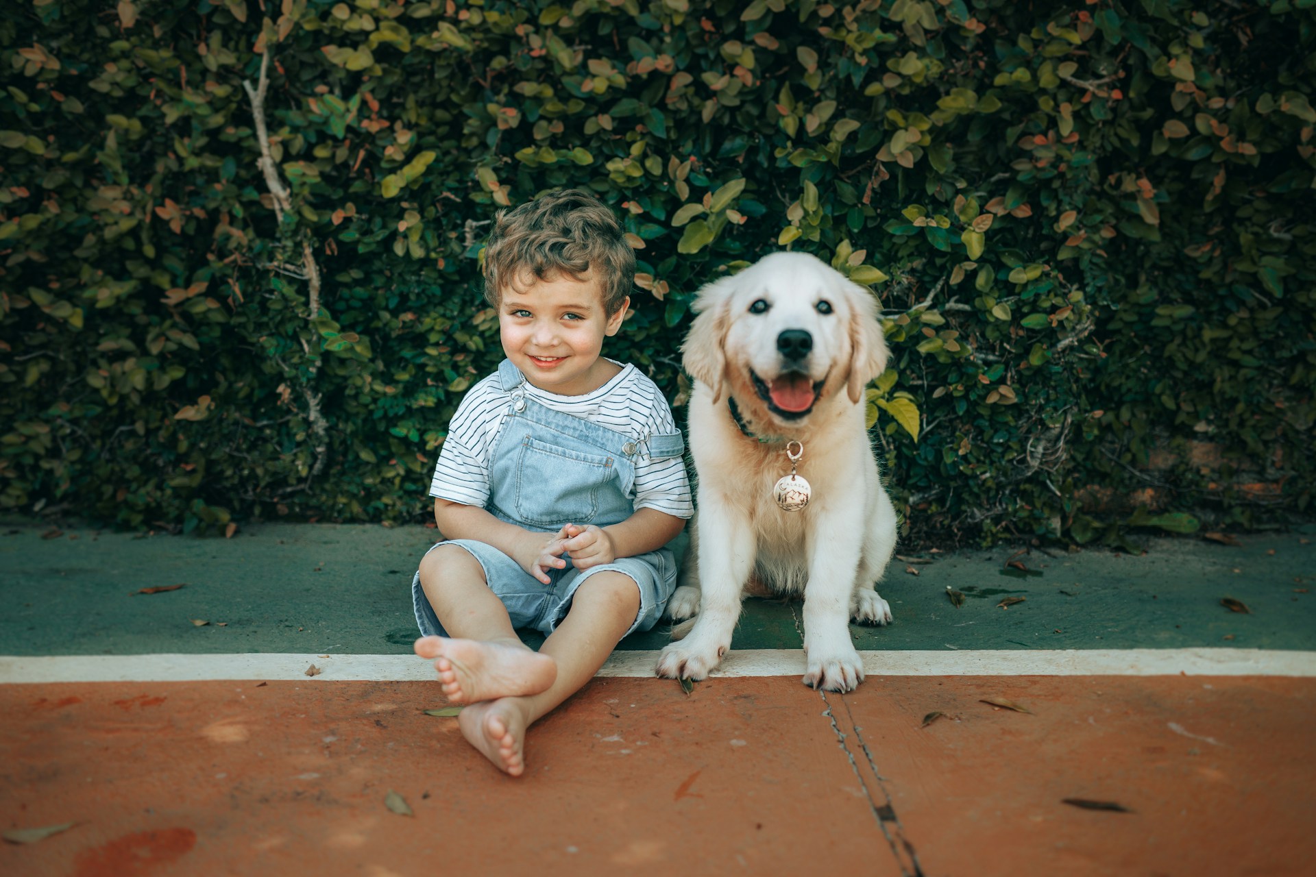 A smiling boy and a golden retriever puppy sit together.