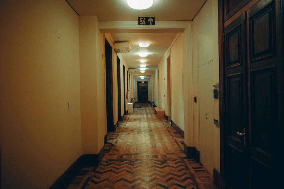 A long hotel hallway lined with identical guest room doors, analogous to a multi-tenant system where every customer looks safely separated until a shared mechanism, like a keycard coded for more than one room, quietly crosses the boundary