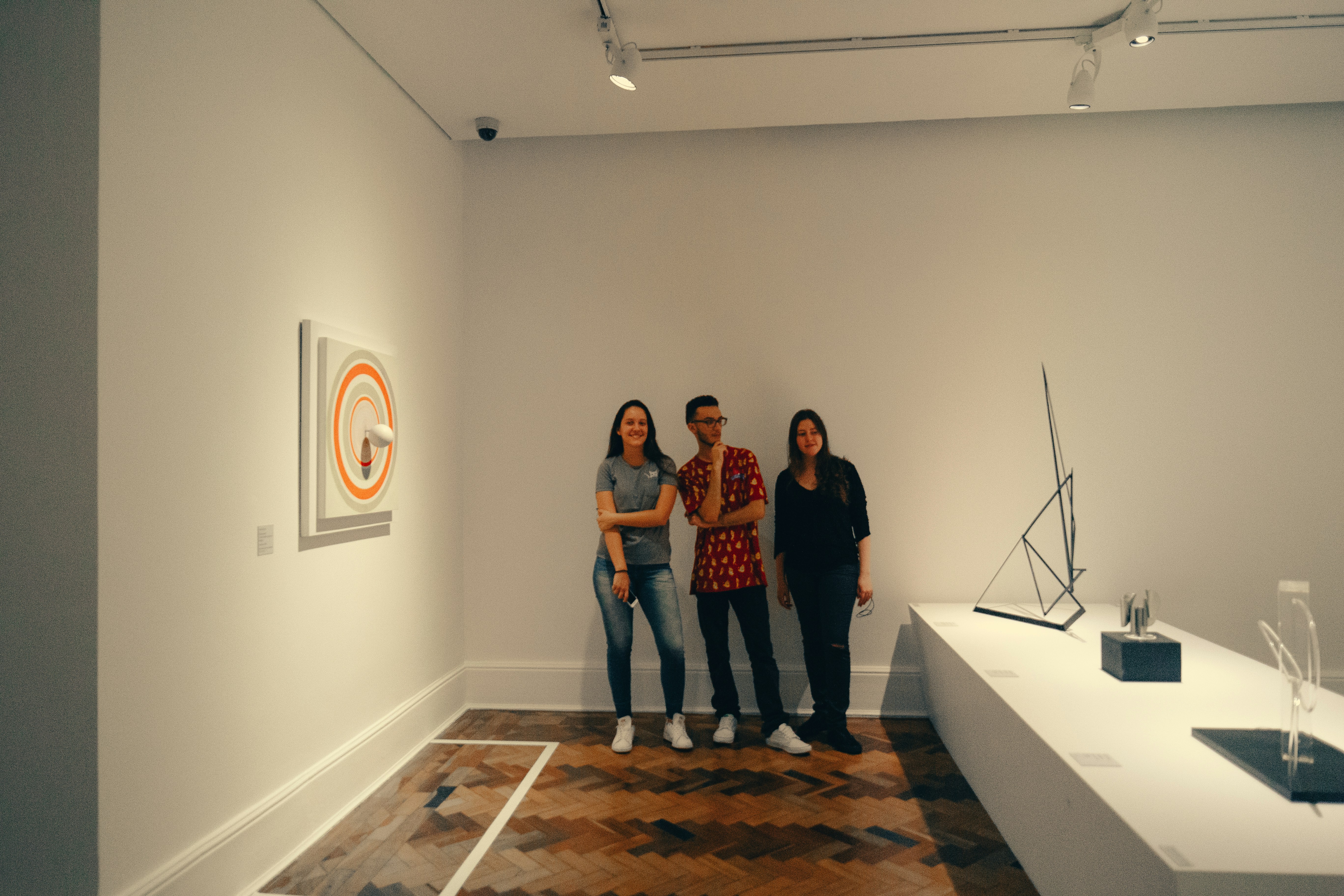 Three people stand in an art gallery exhibition.