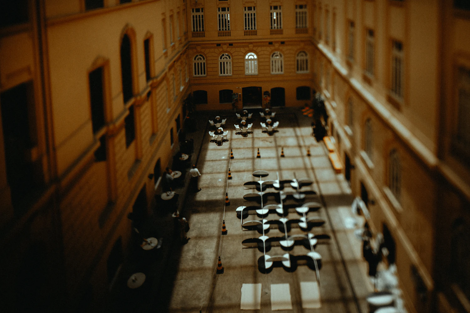 A stone courtyard photographed from an upper window, café chairs and tables stacked and set out in rows below