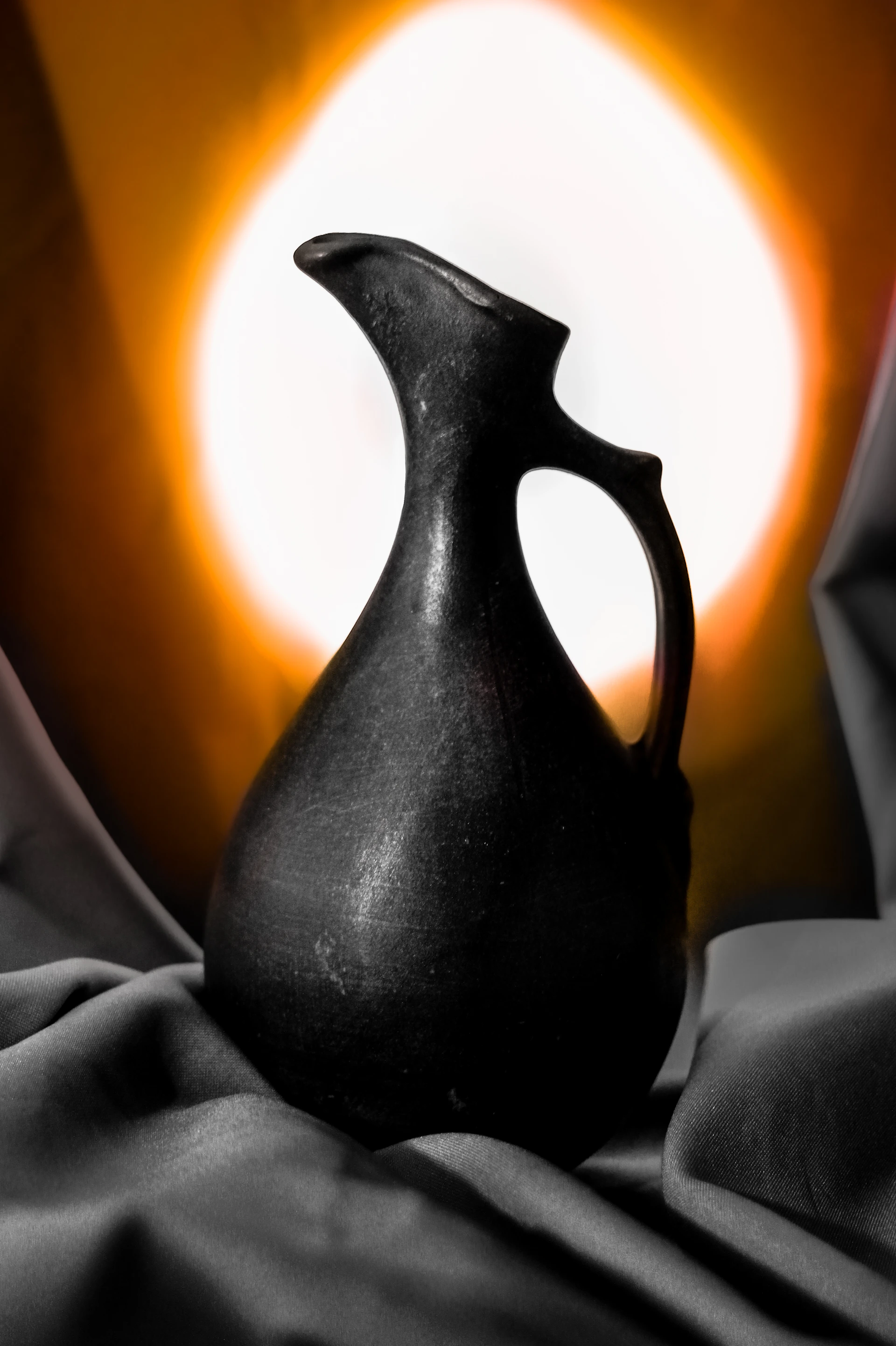 A dark, antique jug sits on draped fabric.