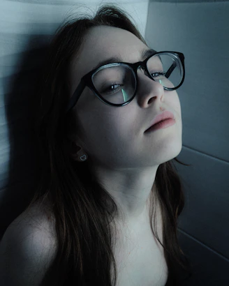 Young woman with glasses looking up thoughtfully.