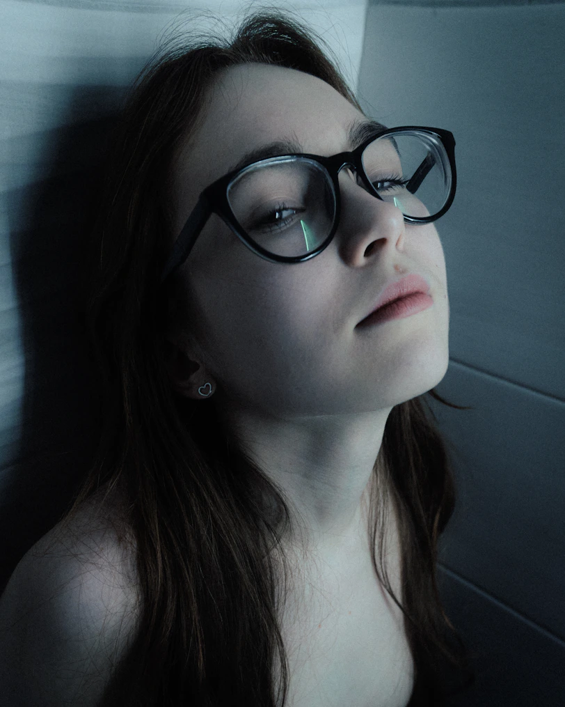 Young woman with glasses looking up thoughtfully.
