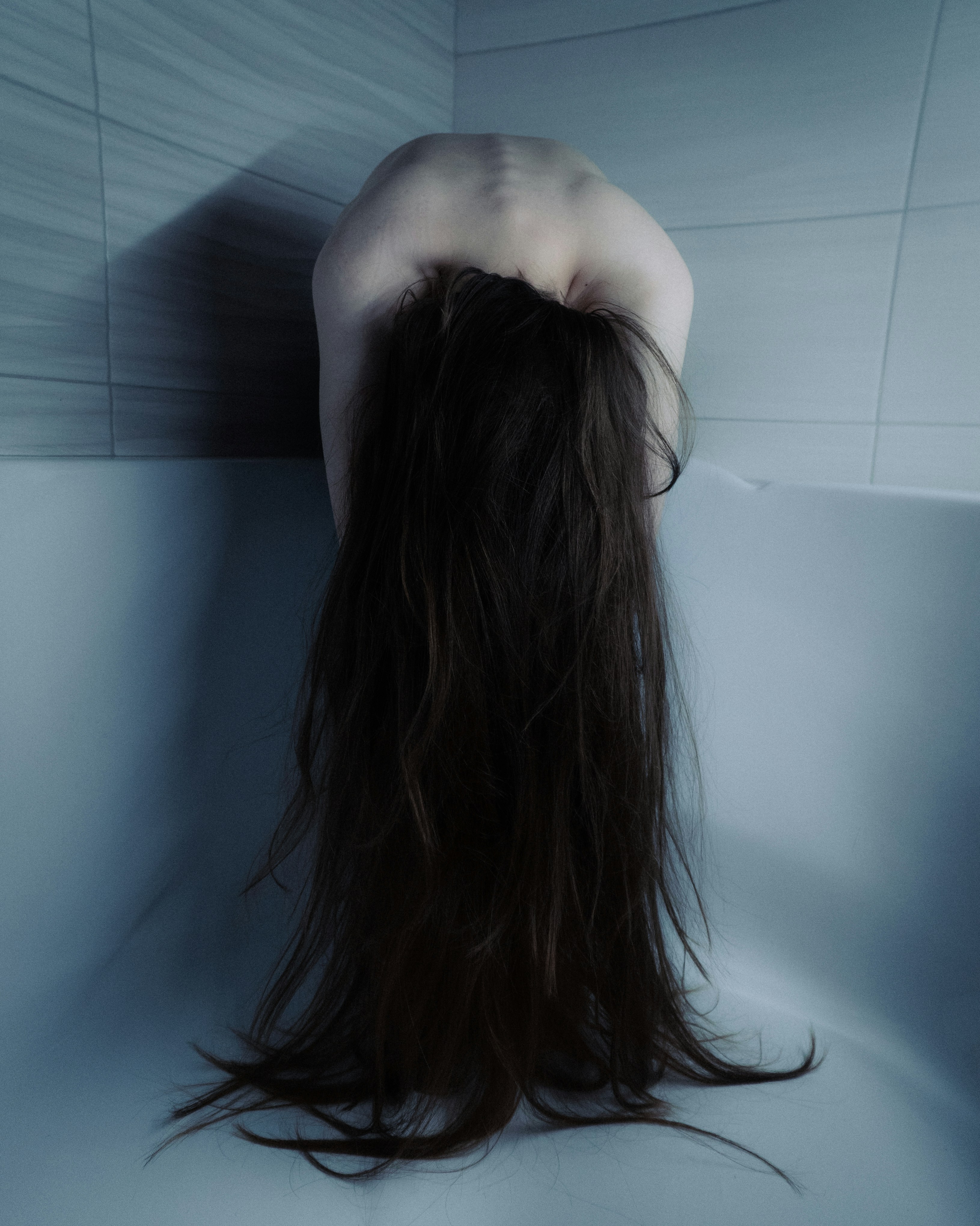 Woman with long hair bent over in bathtub