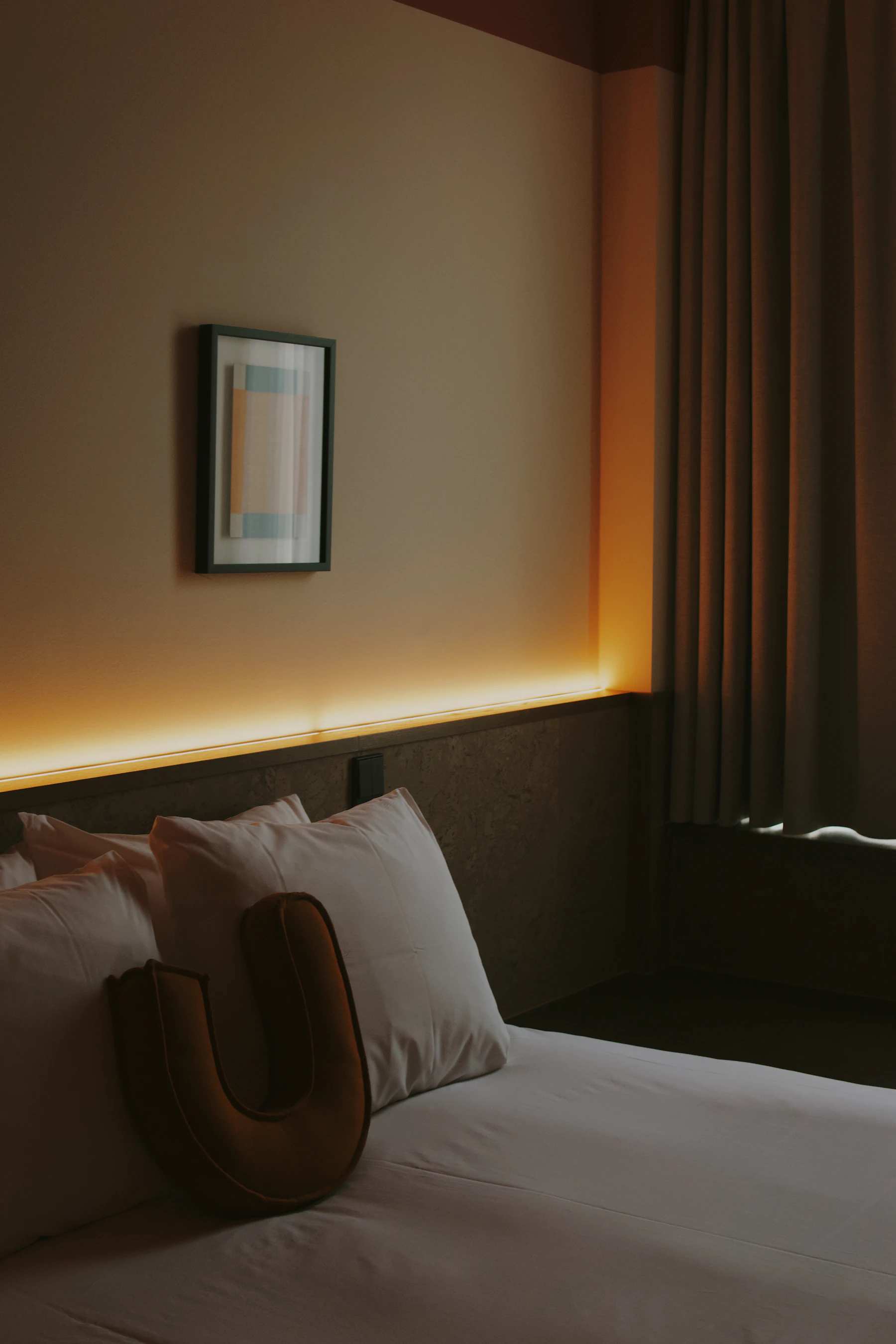 Hidden amber light strip glowing softly behind a bedroom headboard at night