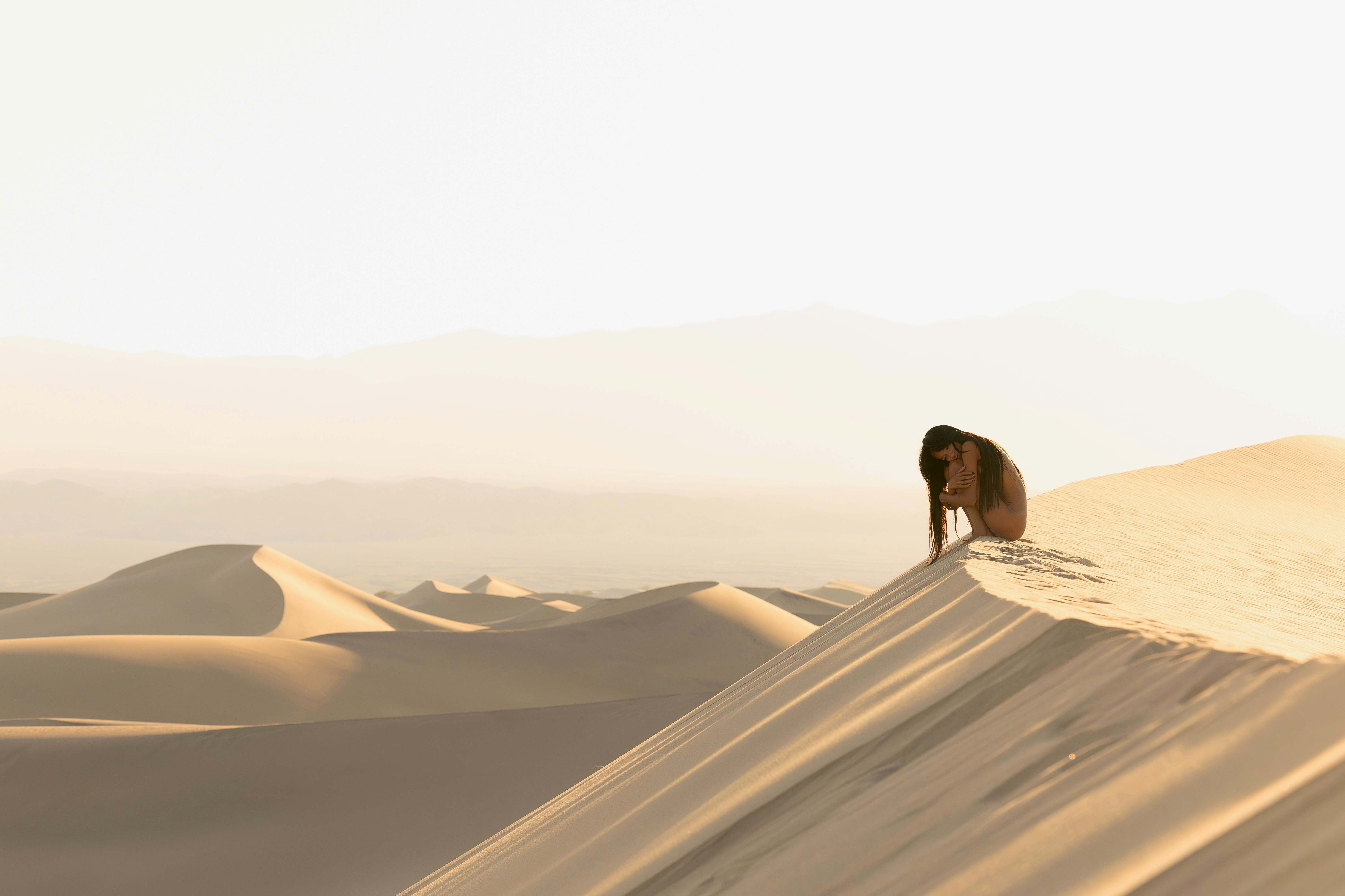 夕暮れの砂丘に一人の姿が座っている。