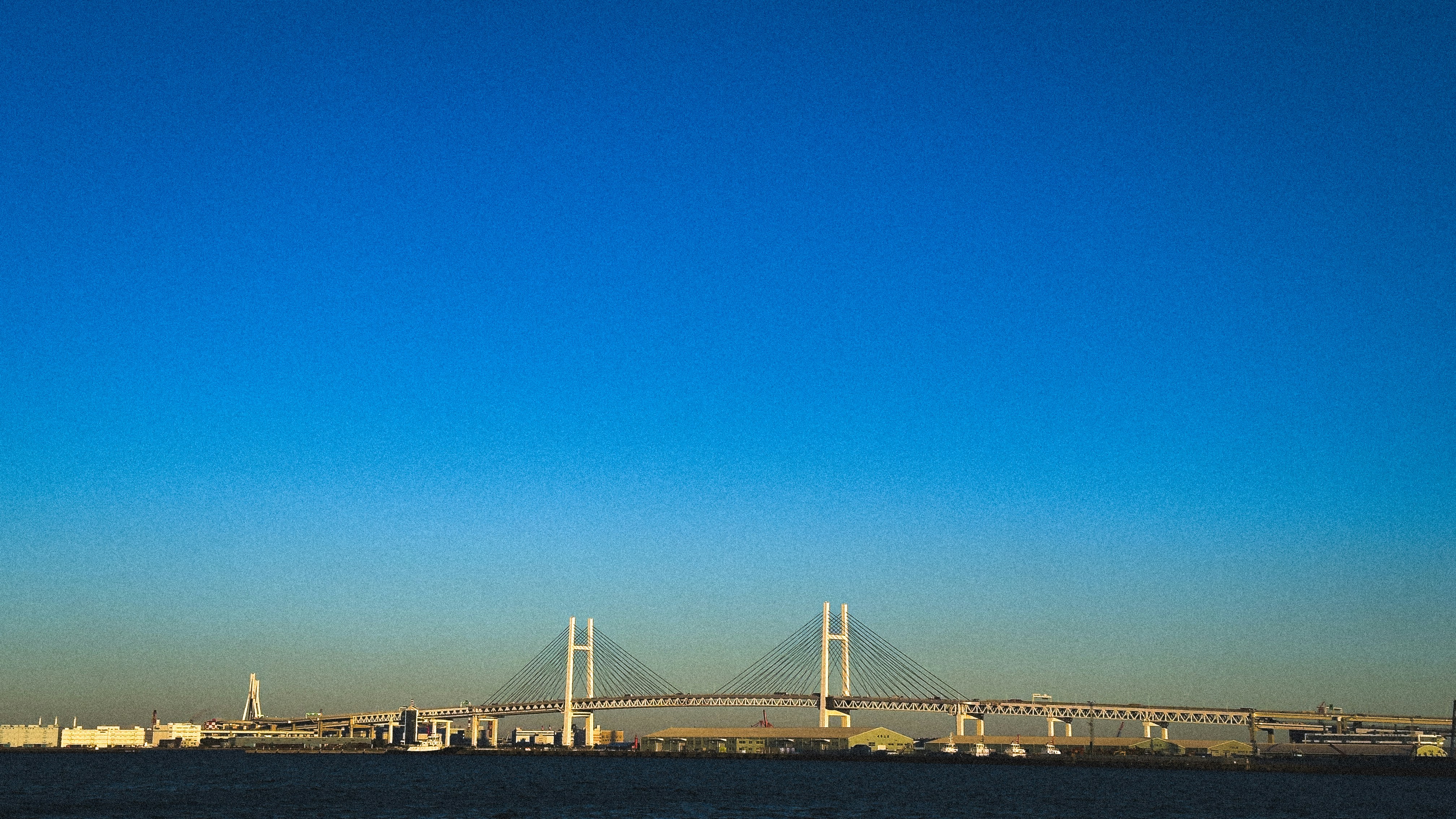 A bright blue sky over a modern bridge and harbor.
