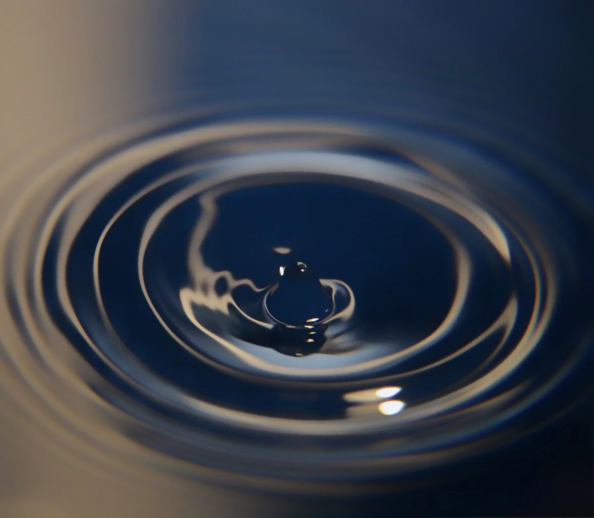 A water drop creating concentric ripples on a dark surface