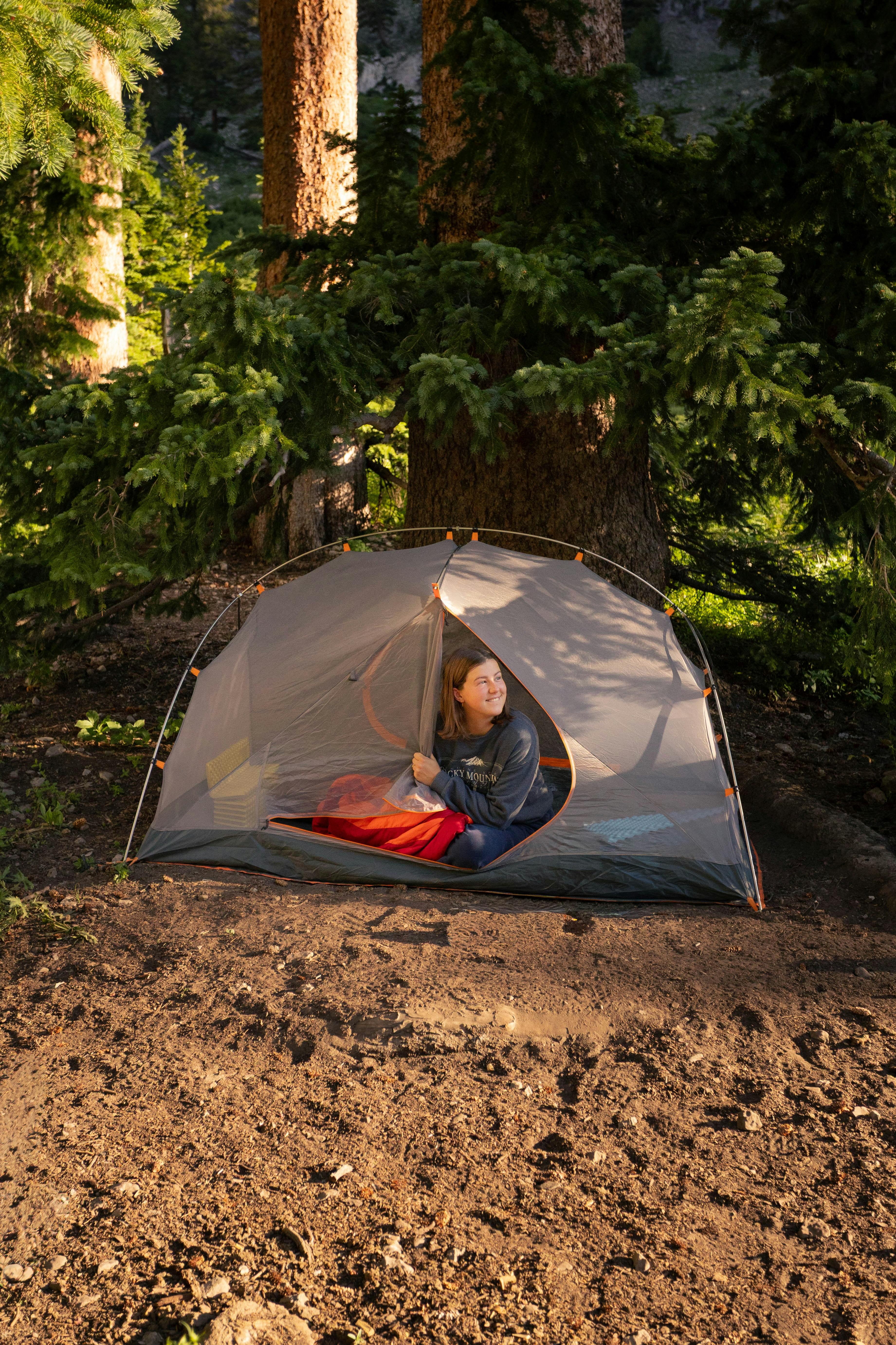 Woman peeking out of a tent in a forest.