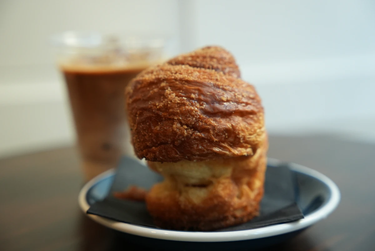 A sugar-crusted croissant on a plate with an iced drink behind it
