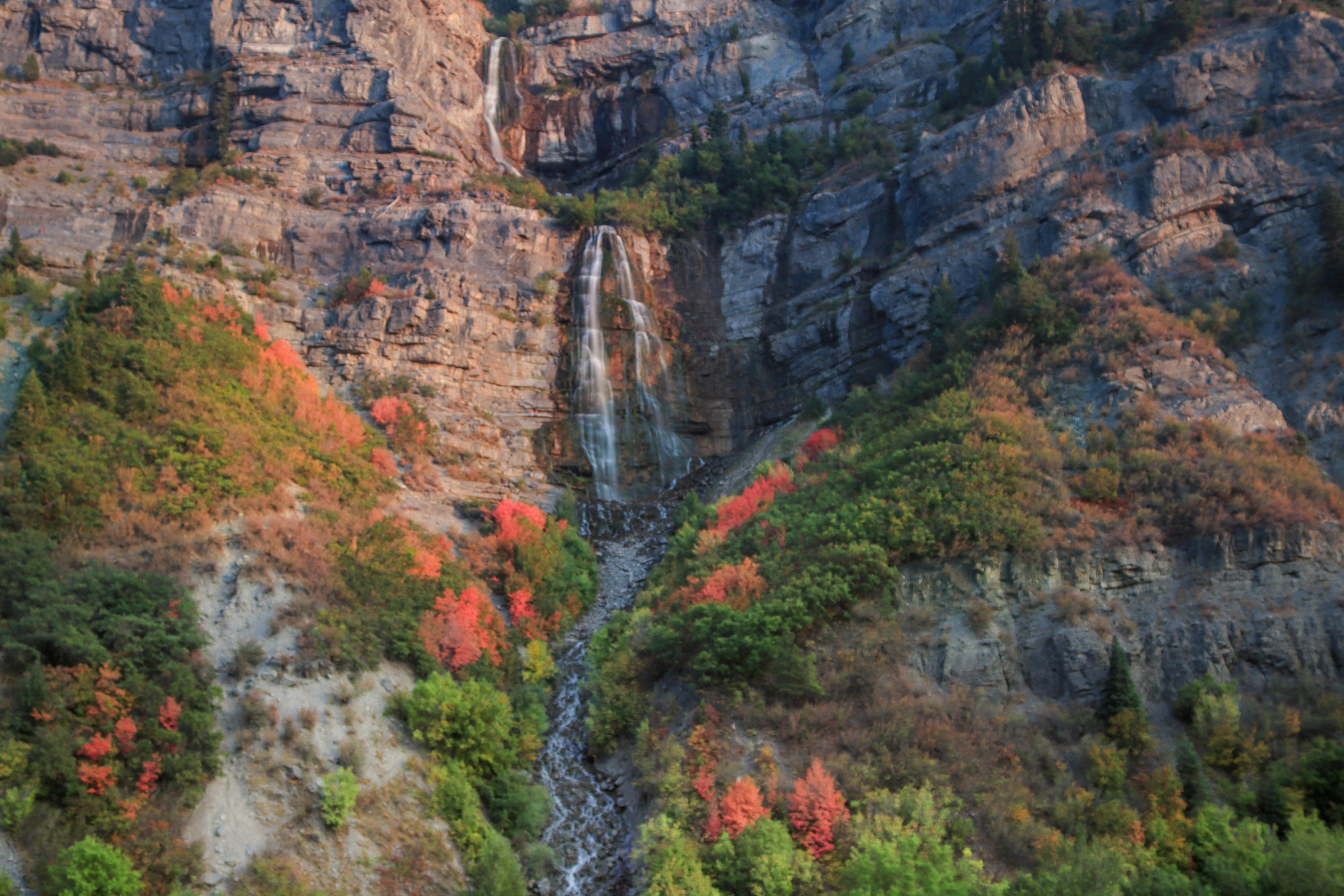 Tall waterfalls cascade down a rocky mountain with autumn foliage.