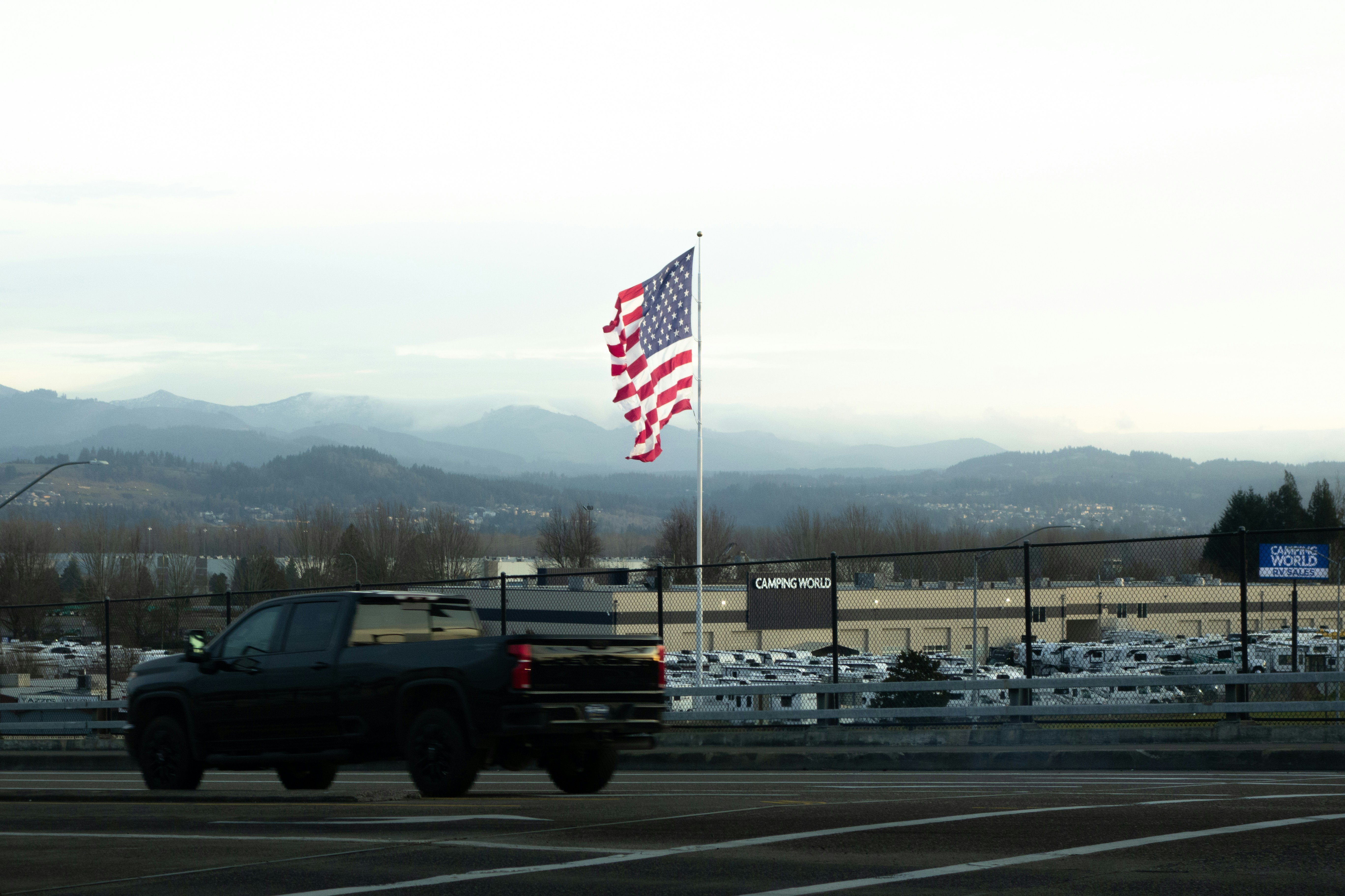 American flag waves near a dark truck and mountains.