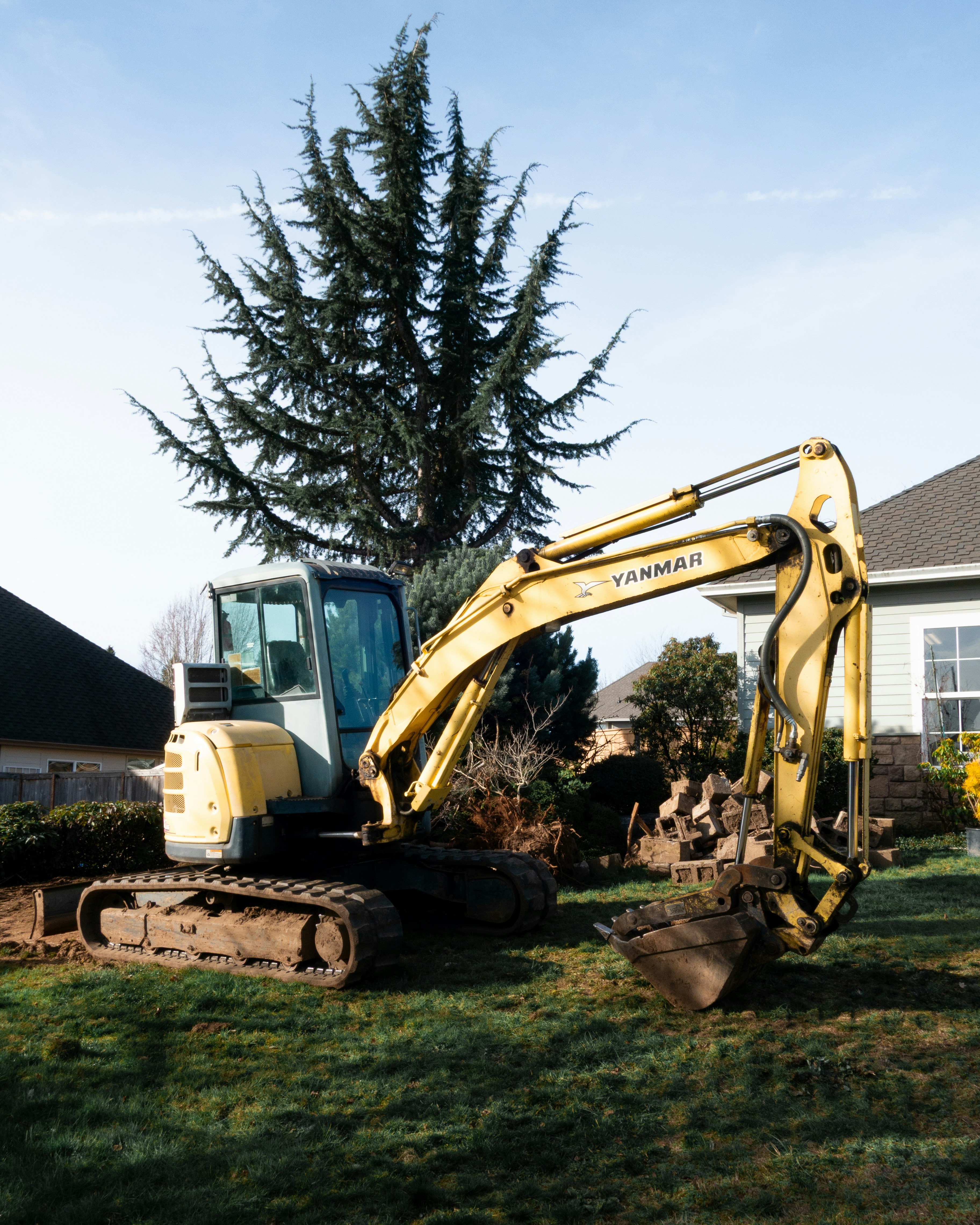 Yellow excavator parked on grassy lawn near houses.