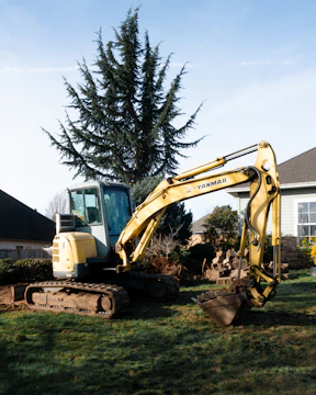 Yellow excavator parked on grassy lawn near houses.