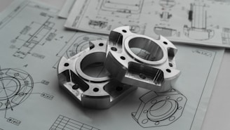 Two metal mechanical parts on engineering blueprints