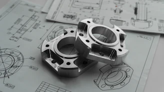 Two metal mechanical parts on engineering blueprints