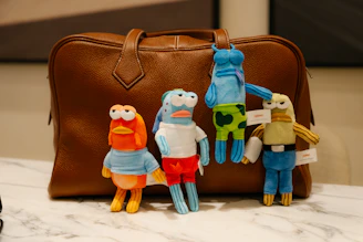 Four plush toys in front of a brown leather bag