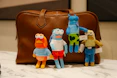 Four plush toys in front of a brown leather bag