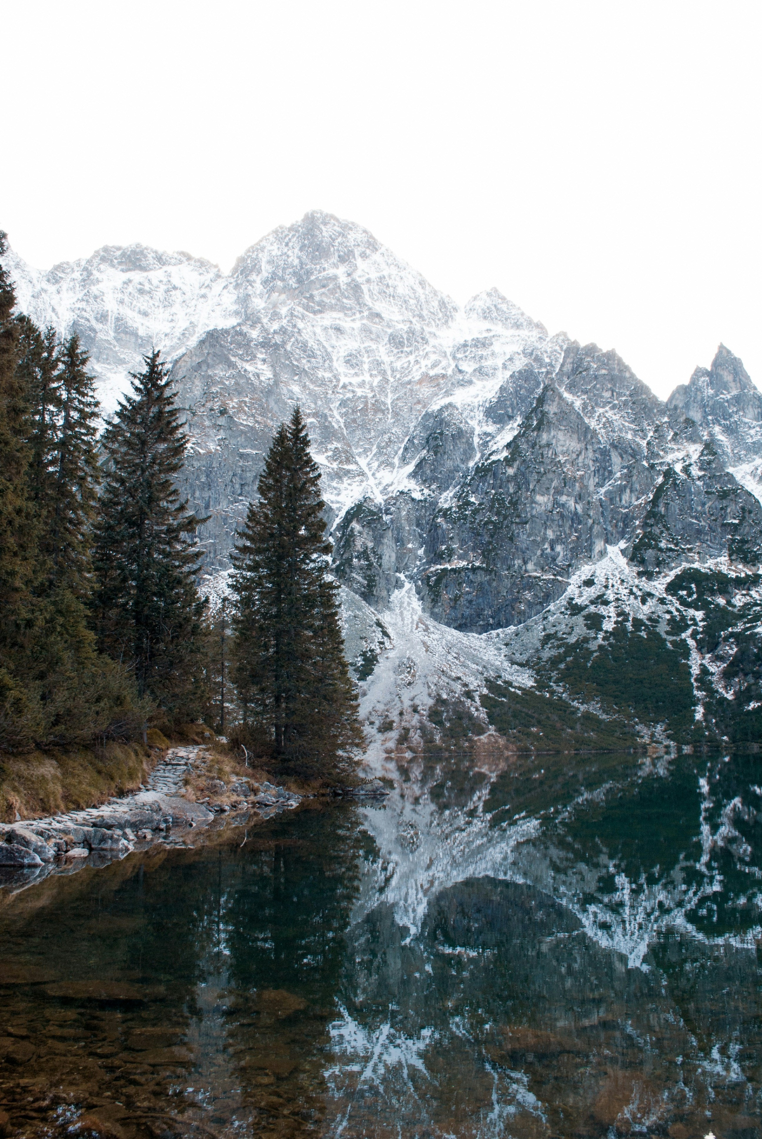 Montanhas nevadas refletidas em um lago calmo com pinheiros
