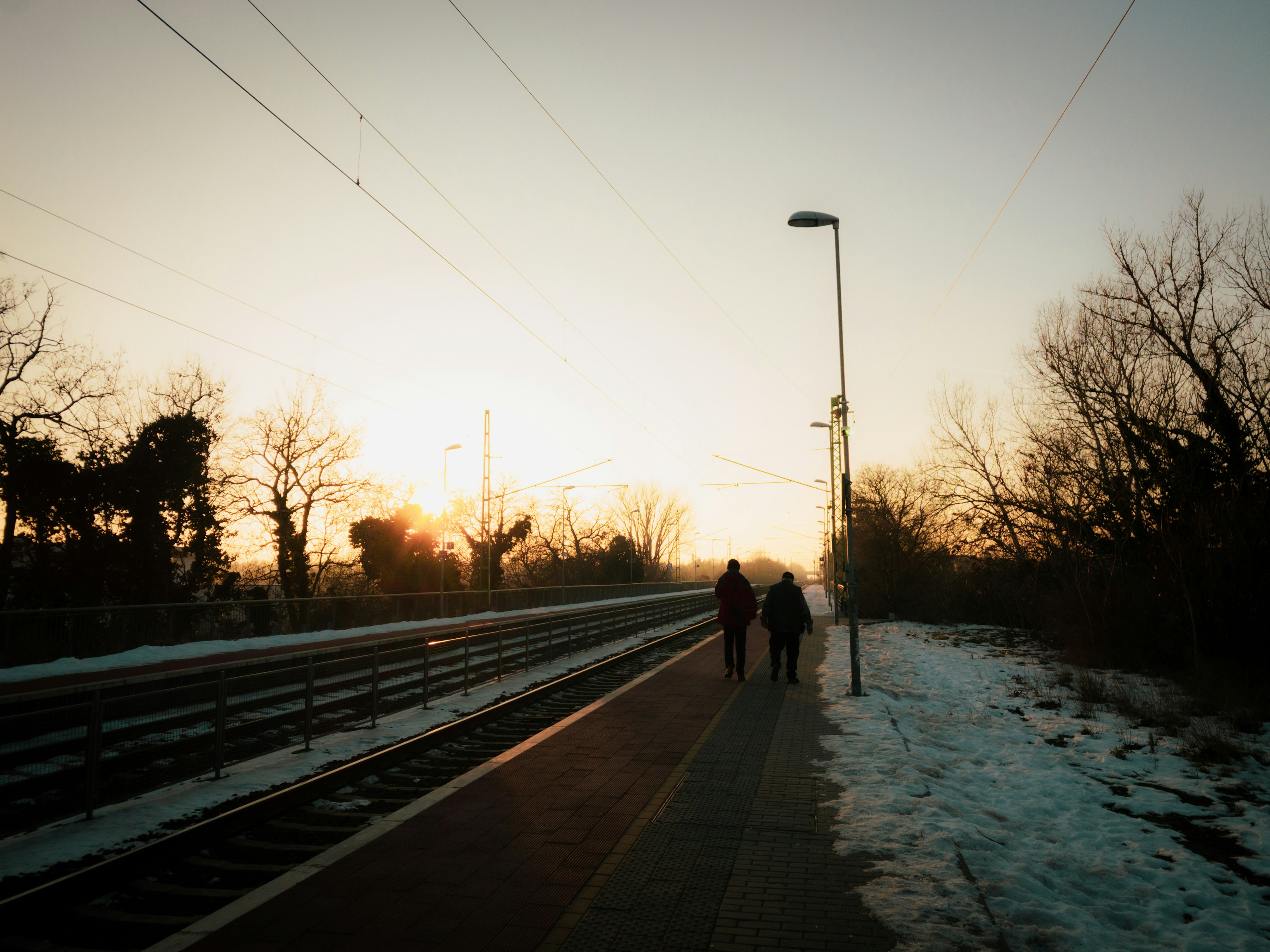 Dos figuras caminan por un andén nevado al atardecer.