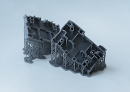 Two gray 3D printed objects with intricate supports