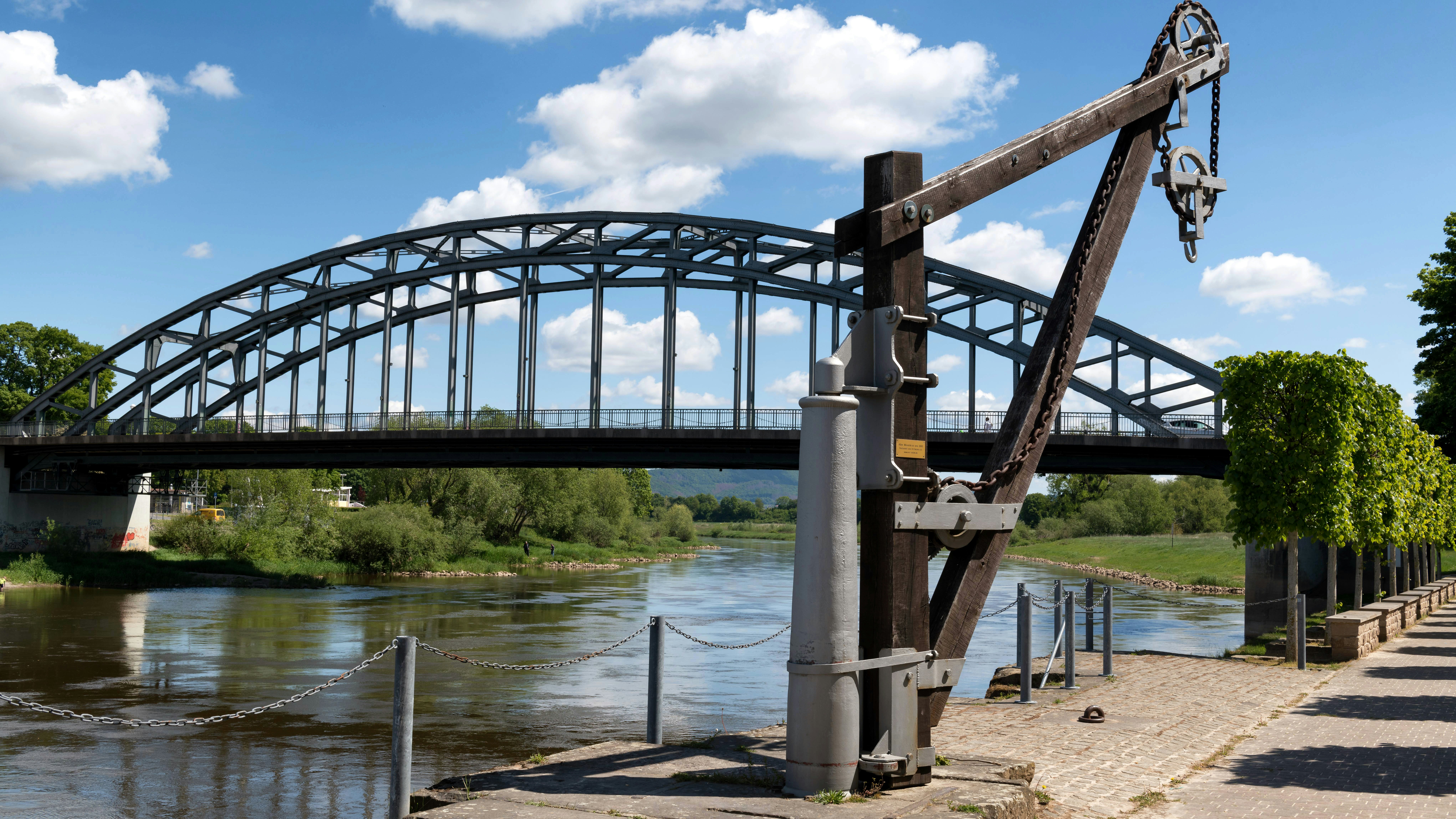 Old wooden crane by river with arched bridge background