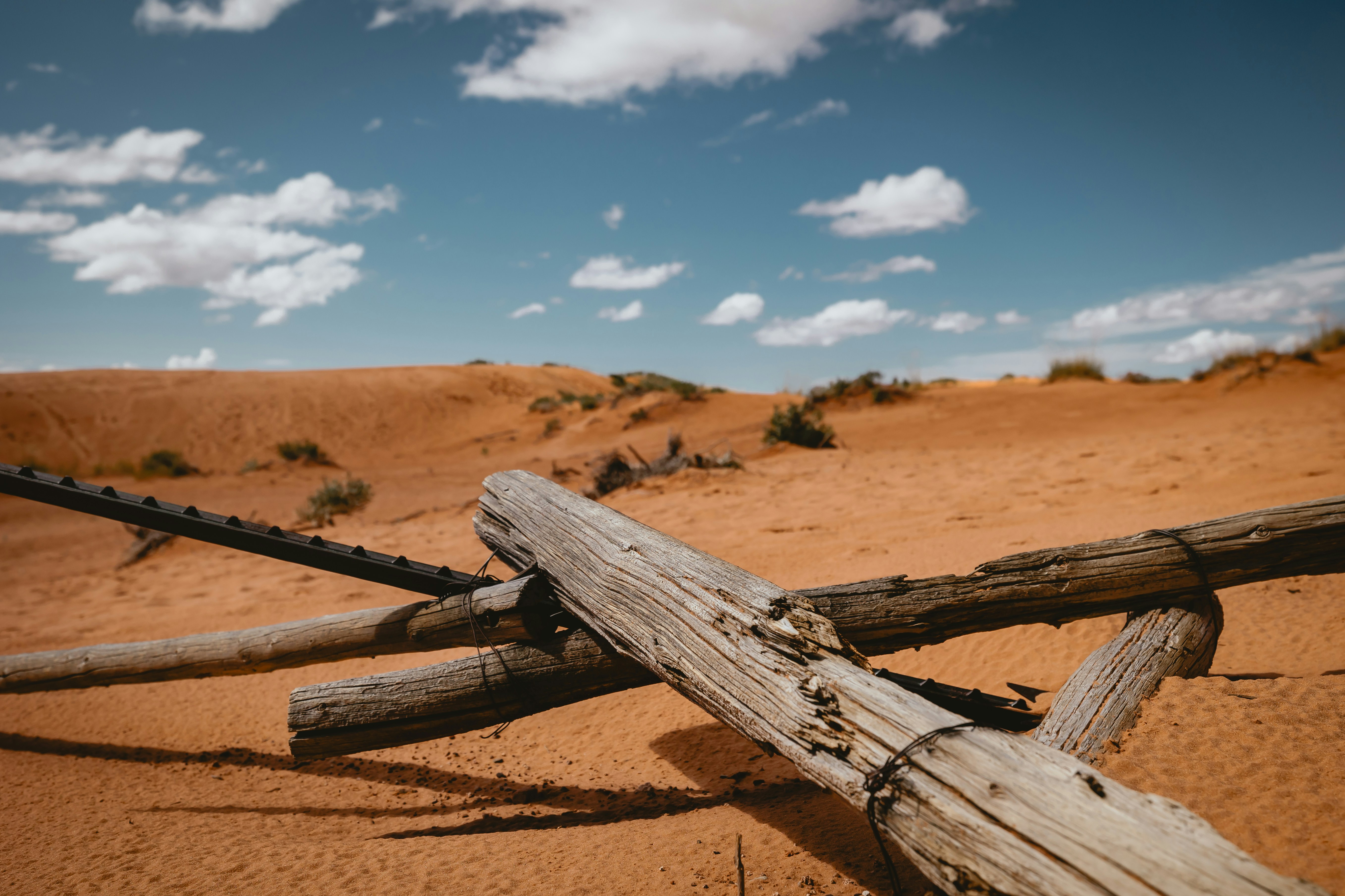 Verwitterter Holzzaun in einer sandigen Wüstenlandschaft.