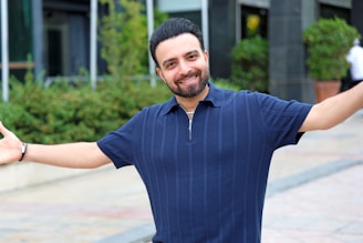 A smiling man with arms outstretched outdoors