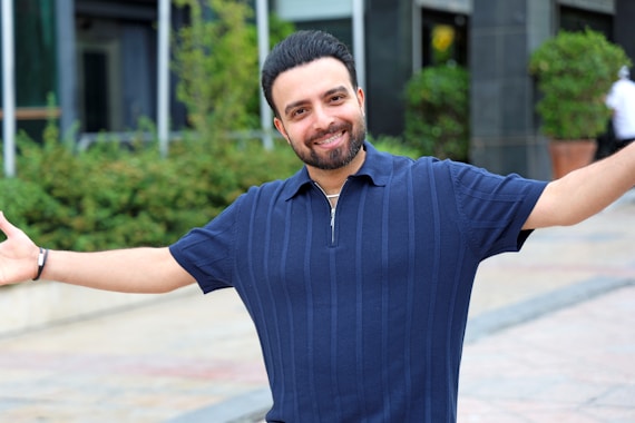 A smiling man with arms outstretched outdoors