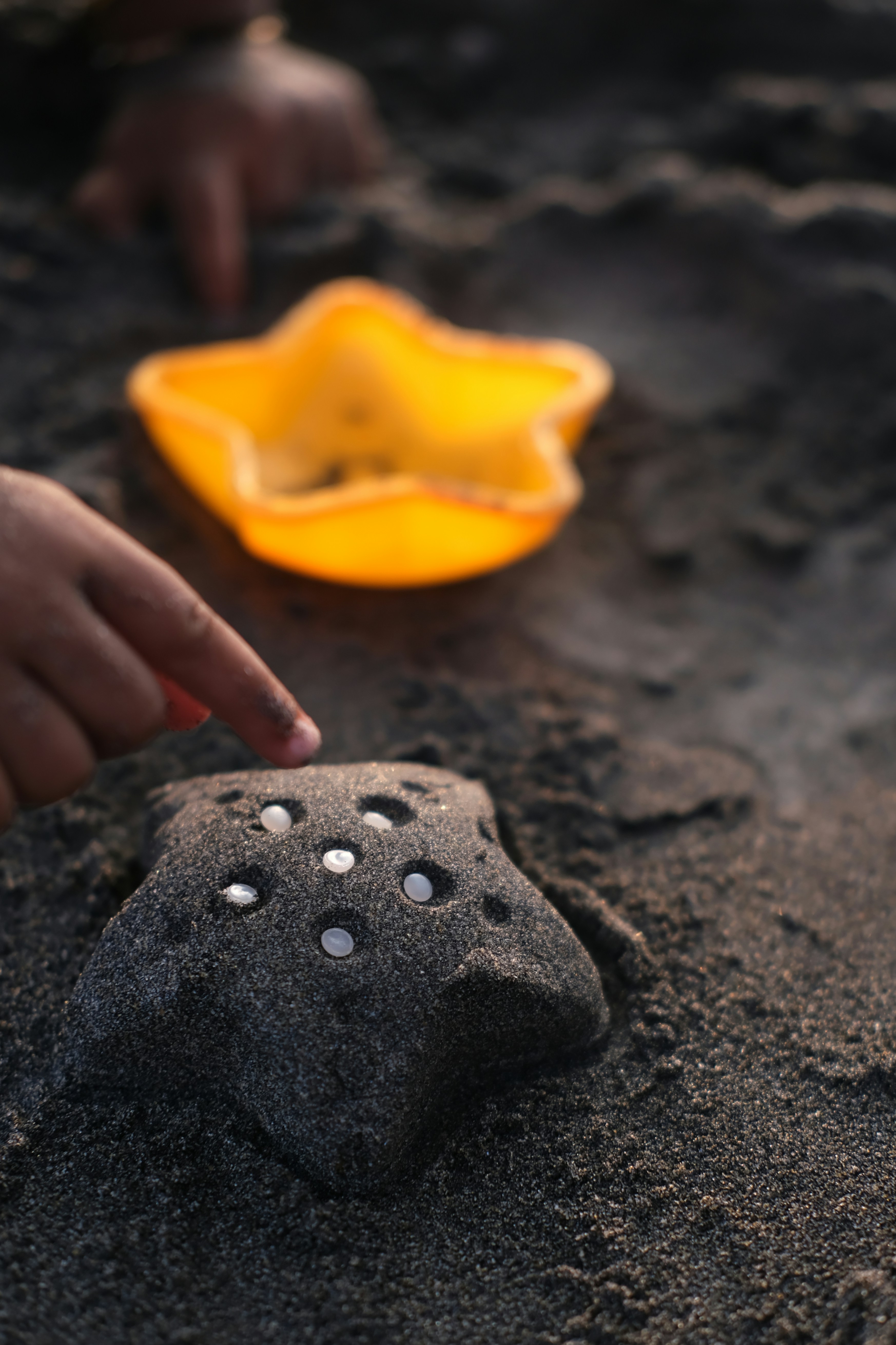 Child's finger points to star-shaped sand mold with pebbles.